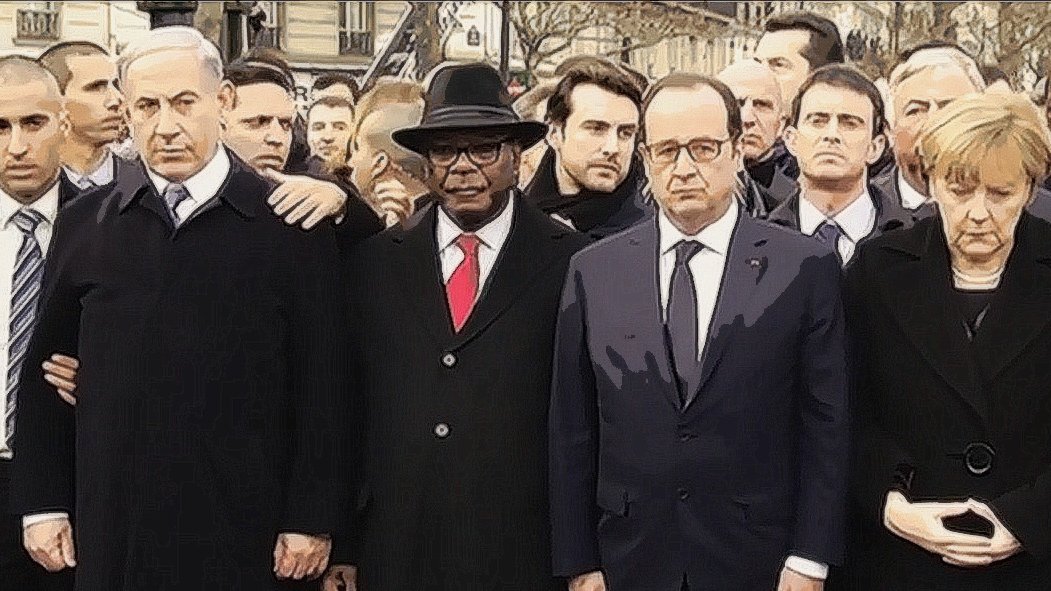 L'image montre un groupe de personnes en émoi, rassemblées dans un cadre public, probablement lors d'un événement solennel. On peut y voir des figures politiques en costumes, dont certaines portent des démarches sérieuses et concentrées. L'ambiance semble être empreinte de gravité et de solidarité. Les participants sont alignés et se regardent, ce qui indique une atmosphère de recueillement ou de soutien mutuel.