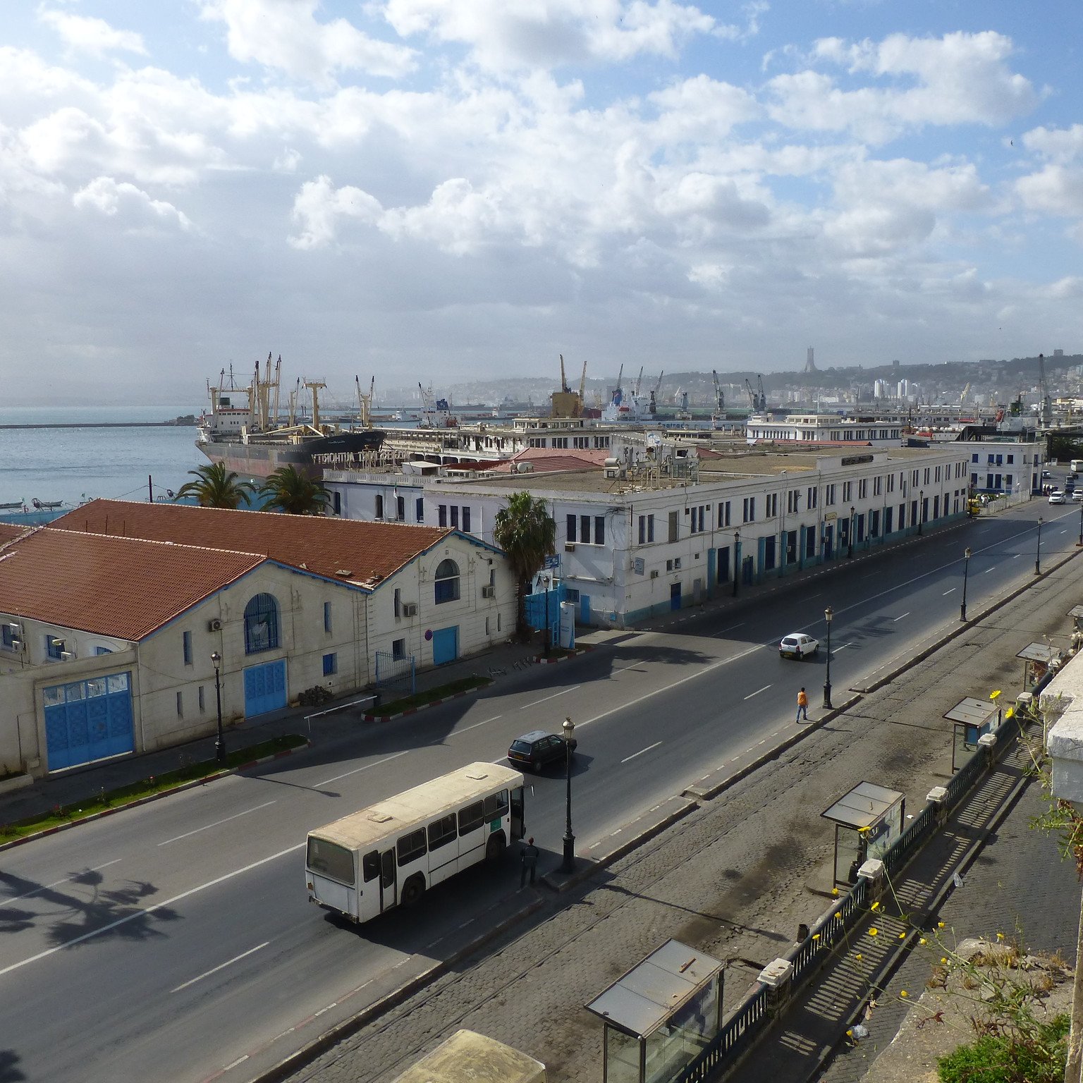 Vue d'une ville côtière avec des bâtiments, port et nuages. Ambiance calme et urbaine.