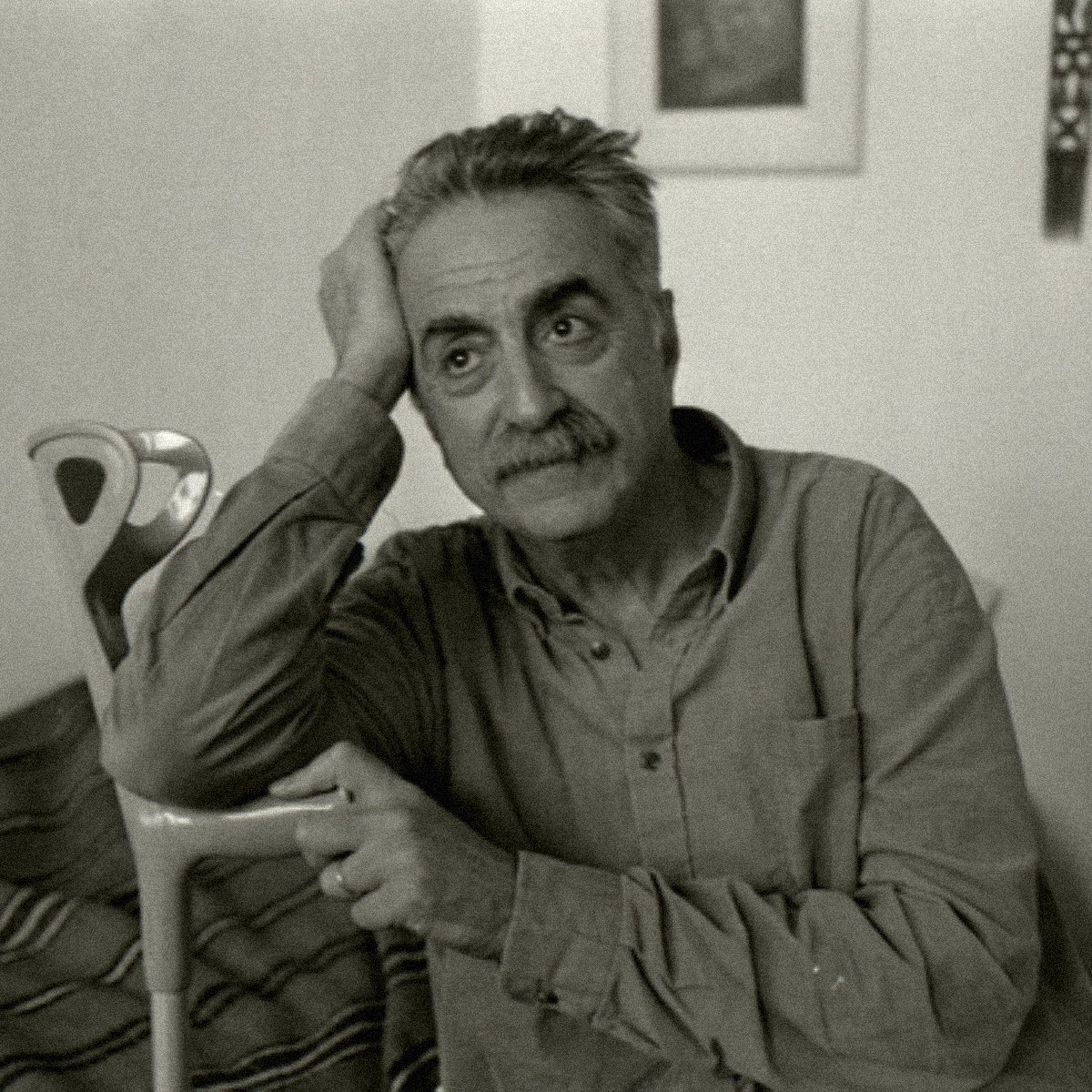 Homme pensif, assis, avec une canne, dans une pièce simple et lumineuse.