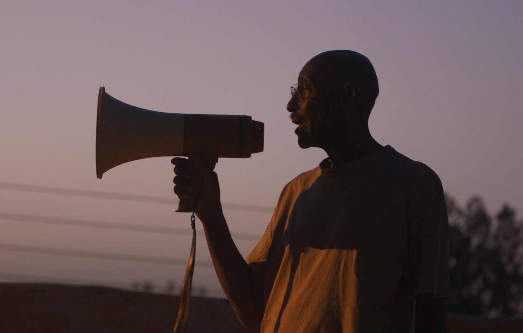 Un homme en silhouette tenant un mégaphone au crépuscule.
