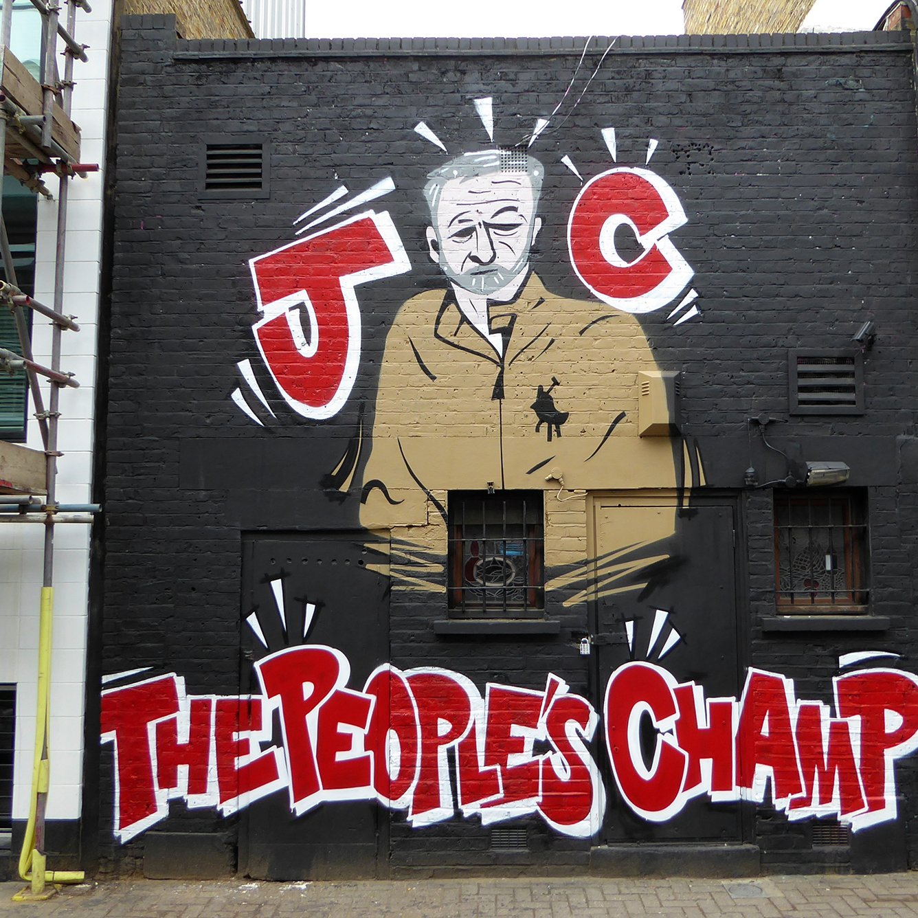 L'image montre un mur décoré d'un graffiti représentant une silhouette d'un homme en costume. Il est entouré de motifs graphiques et de couleurs vives. En bas, on peut lire les mots "THE PEOPLES CHAMP" écrits en lettres grandes et accrocheuses. Le graffiti est caractérisé par un style artistique urbain, typique des œuvres de street art. En arrière-plan, on aperçoit une construction, ajoutant un contexte urbain à l'œuvre.