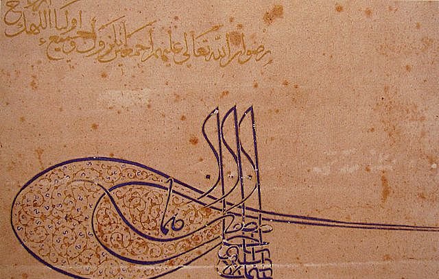 L'image présente un travail calligraphique élaboré, probablement en arabe, qui combine à la fois des mots et des formes artistiques. On observe des lignes fluides et des motifs détaillés, créant une composition harmonieuse. Le texte semble exprimer un message spirituel ou religieux, mettant en valeur la beauté de la langue arabe à travers l'art de la calligraphie. Les couleurs sont principalement des nuances de brun et de doré, ce qui donne une impression de chaleur et d'élégance.