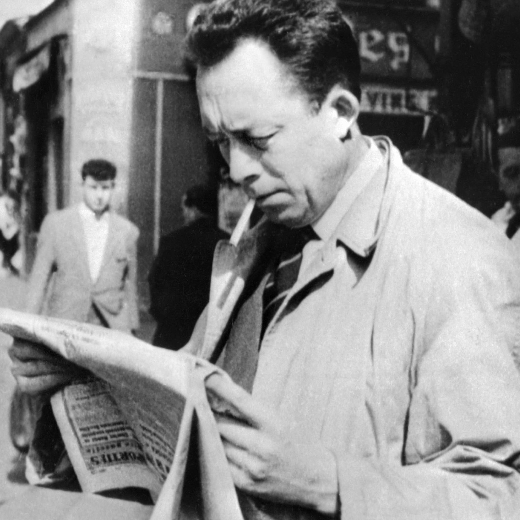 L'image représente un homme dans une rue animée, semblant lire un journal avec attention. Il porte un manteau clair et une cigarette à la bouche. En arrière-plan, on peut voir d'autres passants et des commerces, ce qui donne une ambiance des années passées. La scène évoque une atmosphère de réflexion et d'intérêt pour l'actualité.
