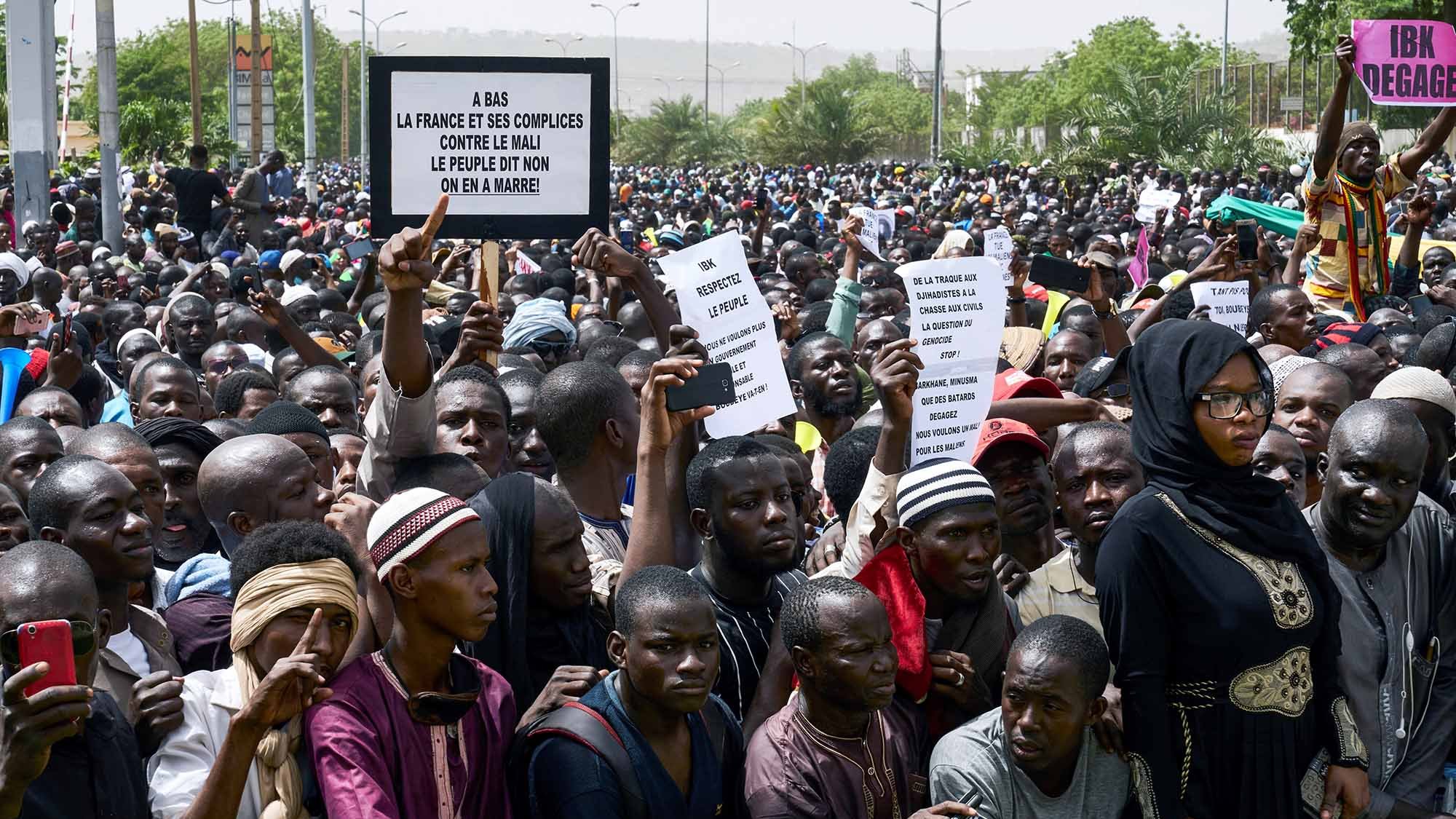 تظهر في الصورة حشود كبيرة من الناس gathered في مظاهرة. يبدو أن هناك شعارات وأوراق يحملها بعض المتظاهرين، تعبر عن مطالب أو احتجاجات معينة. يرتدي البعض ملابس تقليدية، بينما يظهر آخرون بملابس عصرية. يمكن رؤية تفاعل كثيف بين الحضور، مما يبرز حماسهم واهتمامهم بالقضية المطروحة. خلفية الصورة تضم أشجارًا ومبانٍ، مما يدل على أن المظاهرة تحدث في منطقة حضرية.