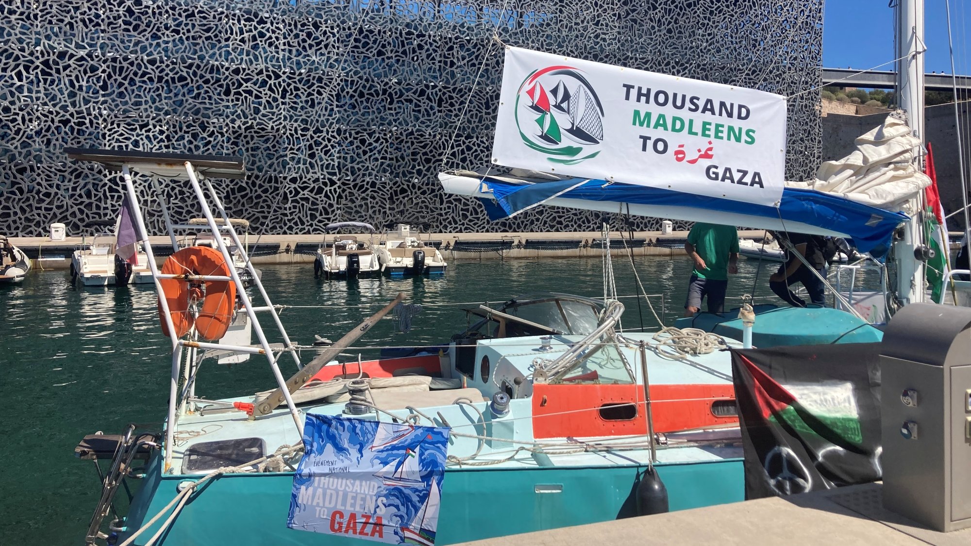Un bateau avec une banderole "Thousand Madleen to Gaza" dans un port moderne.