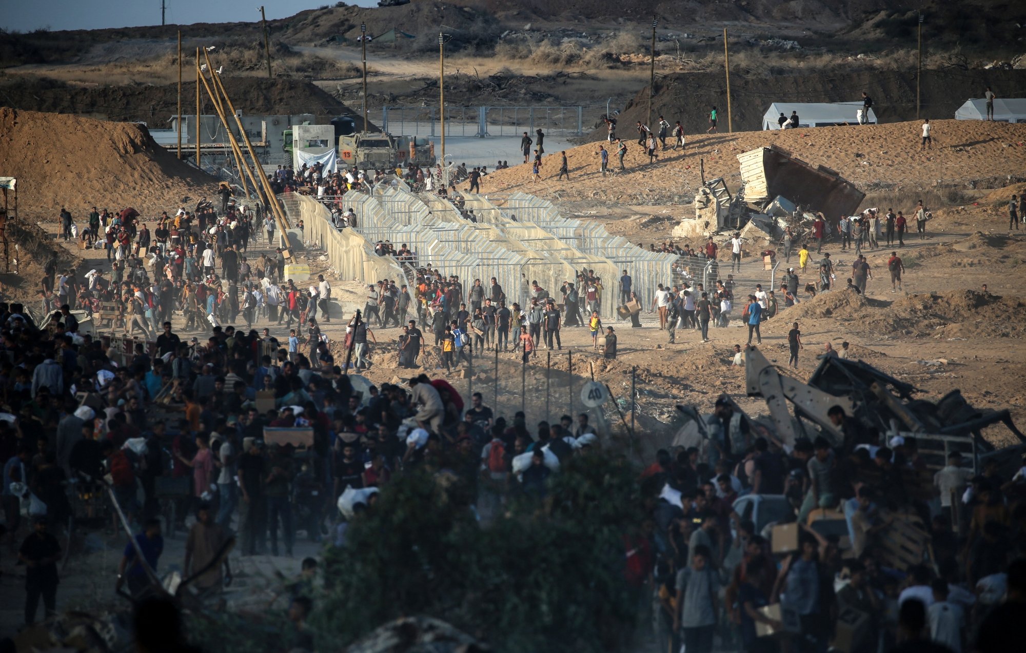 Persone in movimento vicino a barriere in un paesaggio arido e affollato.