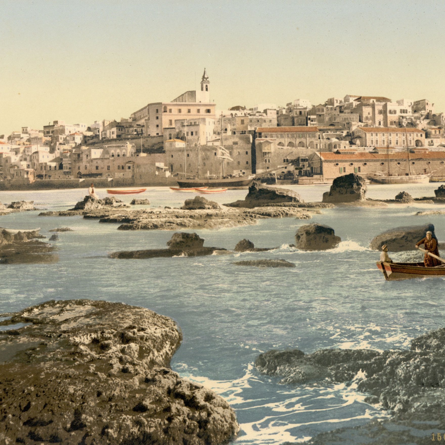 L'image représente un paysage côtier avec une ville en arrière-plan. On peut voir des maisons blanches construisant un front de mer, accompagnées d'une église au sommet d'une colline. Au premier plan, deux personnes naviguent dans un petit bateau sur une eau calme, entouré de rochers. Le ciel est dégagé, suggérant une journée ensoleillée, et la scène évoque une atmosphère paisible et pittoresque. Les couleurs sont vives, mettant en valeur la beauté naturelle de l'endroit.