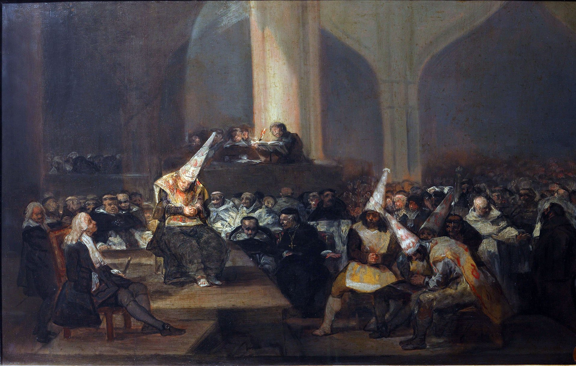 L'image représente une scène dramatique et complexe, typique de l'œuvre de Francisco de Goya. On peut voir un tribunal ou une assemblée où des personnages sont réunis. Au centre, une figure avec un chapeau conique domine la scène, entourée d'autres personnes portant des vêtements sombres. Les expressions sur leurs visages montrent une grande tension et une atmosphère de jugement. La lumière semble être focalisée sur certains personnages, mettant en évidence le caractère sombre et sérieux de la situation. L'arrière-plan est rempli de spectateurs, ajoutant à l'intensité de l'assemblée.