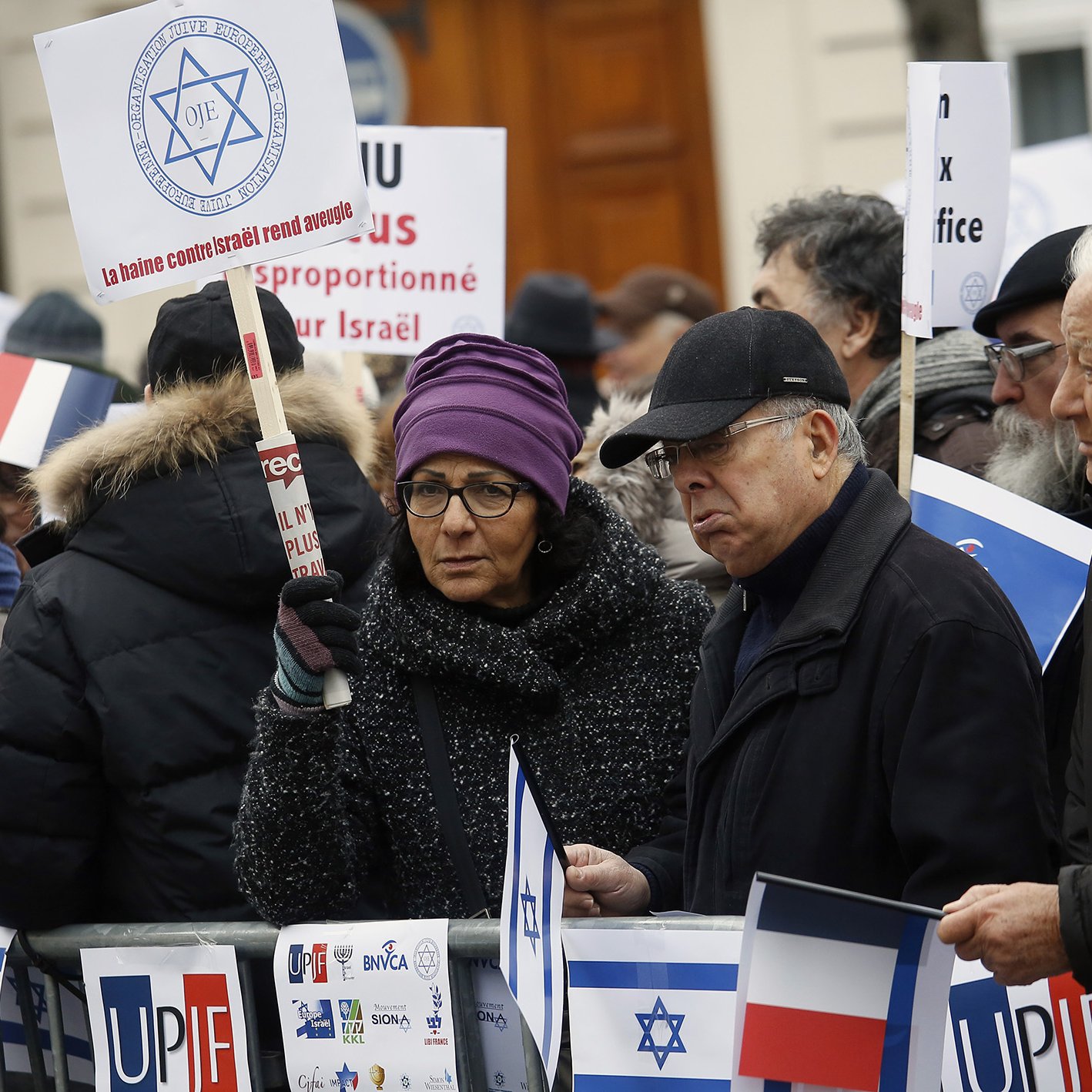 الصورة تظهر مجموعة من الأشخاص في تجمع أو مظاهرة. يحملون لافتات وأعلام، من بينها العلم الإسرائيلي، ويرتدون ملابس شتوية. يبدو أن المتظاهرين يعبرون عن آرائهم حول قضية معينة تتعلق بإسرائيل. المشهد يعكس تفاعل الناس مع قضايا سياسية واجتماعية.