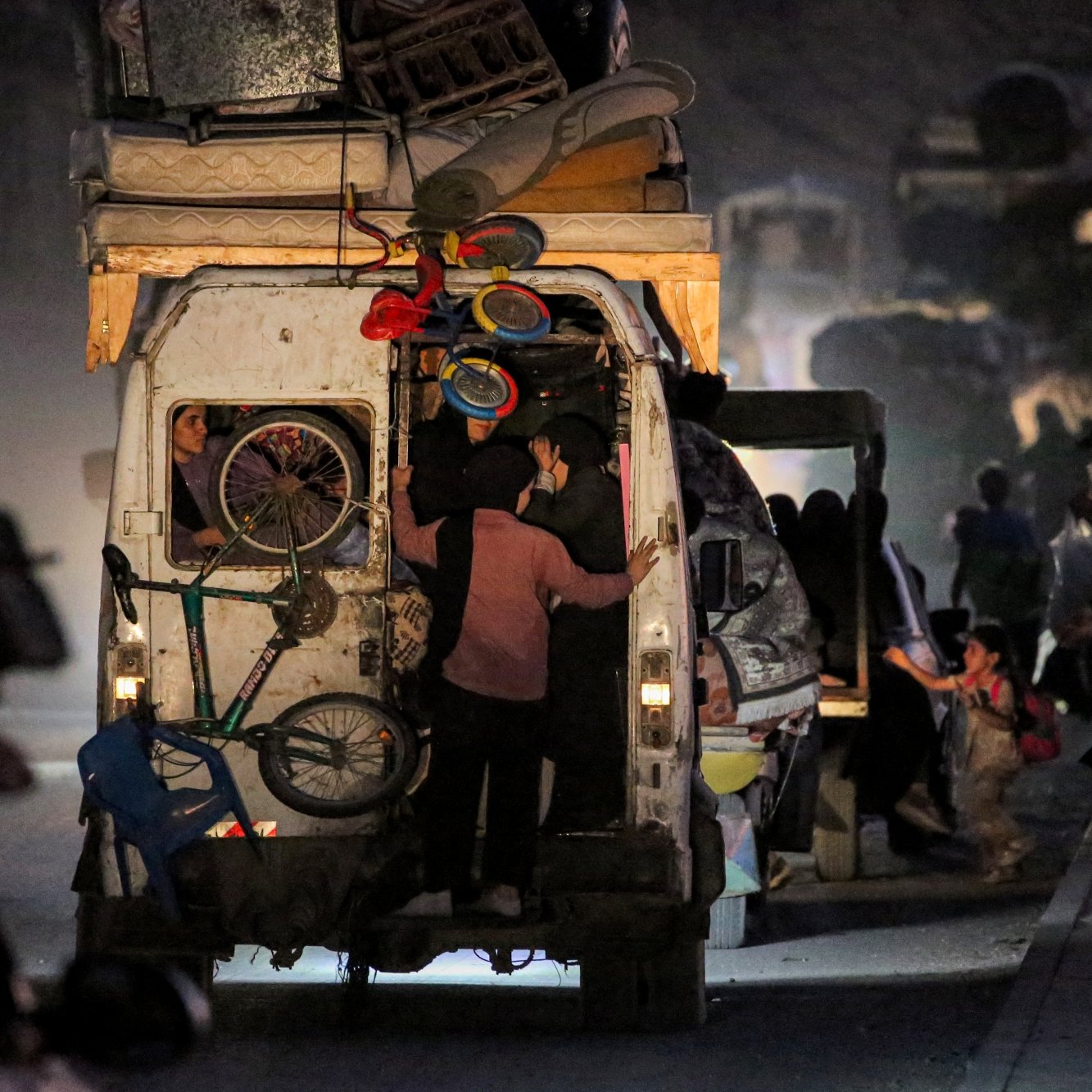 Un furgone pieno di oggetti, persone in movimento in un ambiente polveroso e notturno.