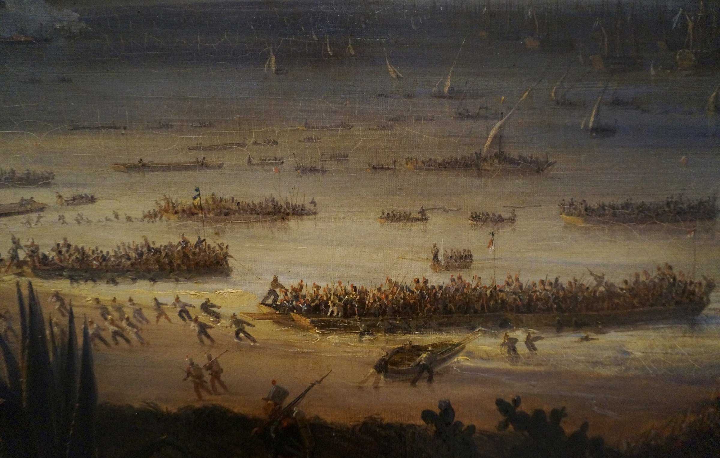 L'image représente une scène de bataille ou de débarquement maritime. On y voit plusieurs bateaux et embarcations sur une étendue d'eau, avec beaucoup de personnes à bord. Sur la rive, des groupes de soldats ou de guerriers semblent se préparer à l'assaut ou à un combat. L'arrière-plan montre des voiliers et des structures, ce qui suggère un port ou une plage animée. L'atmosphère paraît dynamique et chargée d'action, avec des personnages en mouvement, créant une impression de chaos et de détermination.