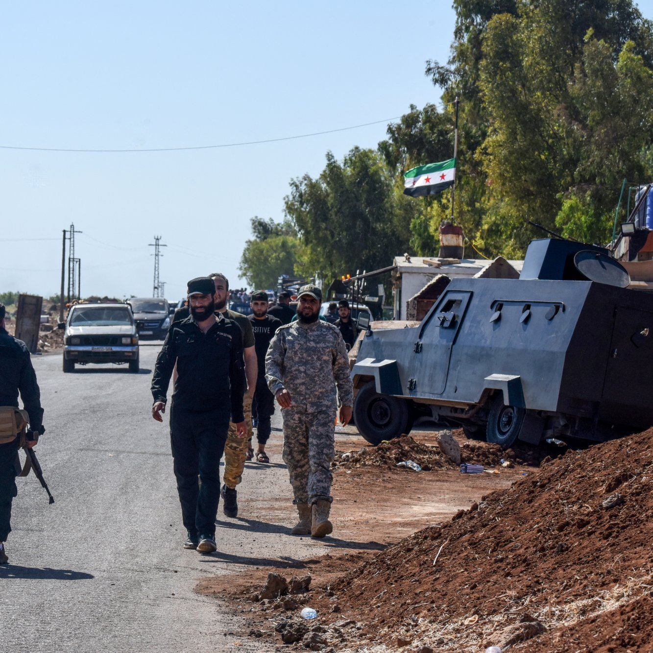 Des soldats marchent le long d'une route, près de véhicules militaires et d'arbres.
