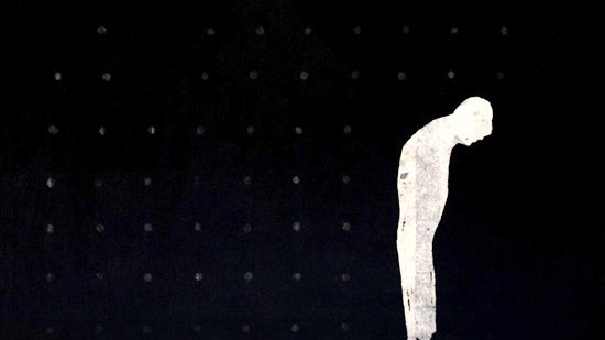 تظهر في الصورة خلفية سوداء داكنة، وفيها شكل أبيض لإنسان واقف. يبدو هذا الشخص مائلًا إلى الأمام، وكأنه يعبر عن الحزن أو الاستسلام. الخلفية تحتوي على نقاط صغيرة، مما يضيف عمقًا للصورة ويجعل التركيز أكثر على الشكل البشري. تعكس الصورة شعور الوحدة أو العزلة من خلال استخدام الألوان والتكوين البسيط.