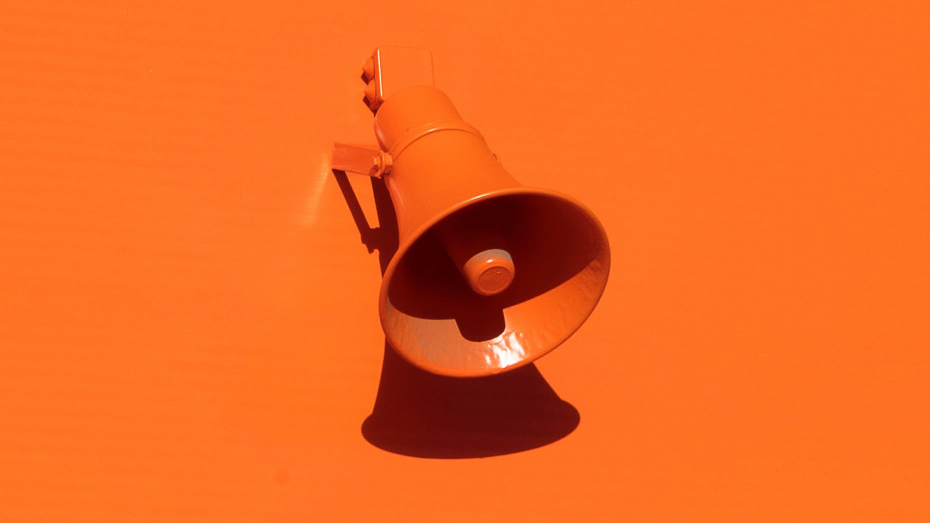الصورة تظهر جرس صوتي ملون باللون البرتقالي، مثبت على حائط بنفس اللون. يبرز الجرس بشكل واضح بفضل تباين الضوء والظل، مما يخلق تأثيرًا جذابًا. الجرس يبدو نظيفًا ومعتنىً به، مما يعكس تصميمًا بسيطًا وحيويًا.