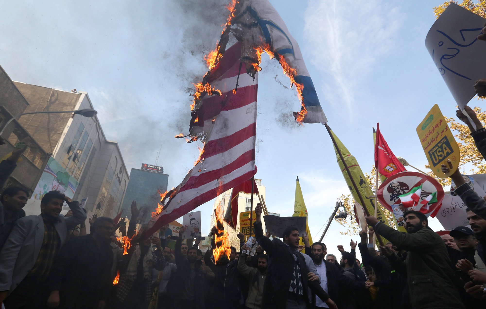 در این تصویر، جمعیتی در حال برگزاری یک تظاهرات هستند. گروهی از افراد در حال آتش زدن پرچم‌هایی با نمادهای مشخص هستند. پشت زمینه تظاهرات، ساختمان‌ها و تابلوهای تبلیغاتی دیده می‌شود. شمار زیادی از تظاهرکنندگان در دست خود پلاکاردهایی نشان می‌دهند که بر روی آن‌ها شعارهایی نوشته شده است. جو عمومی تصویر نشان‌دهندهٔ هیجان و احساسات قوی شرکت‌کنندگان است.