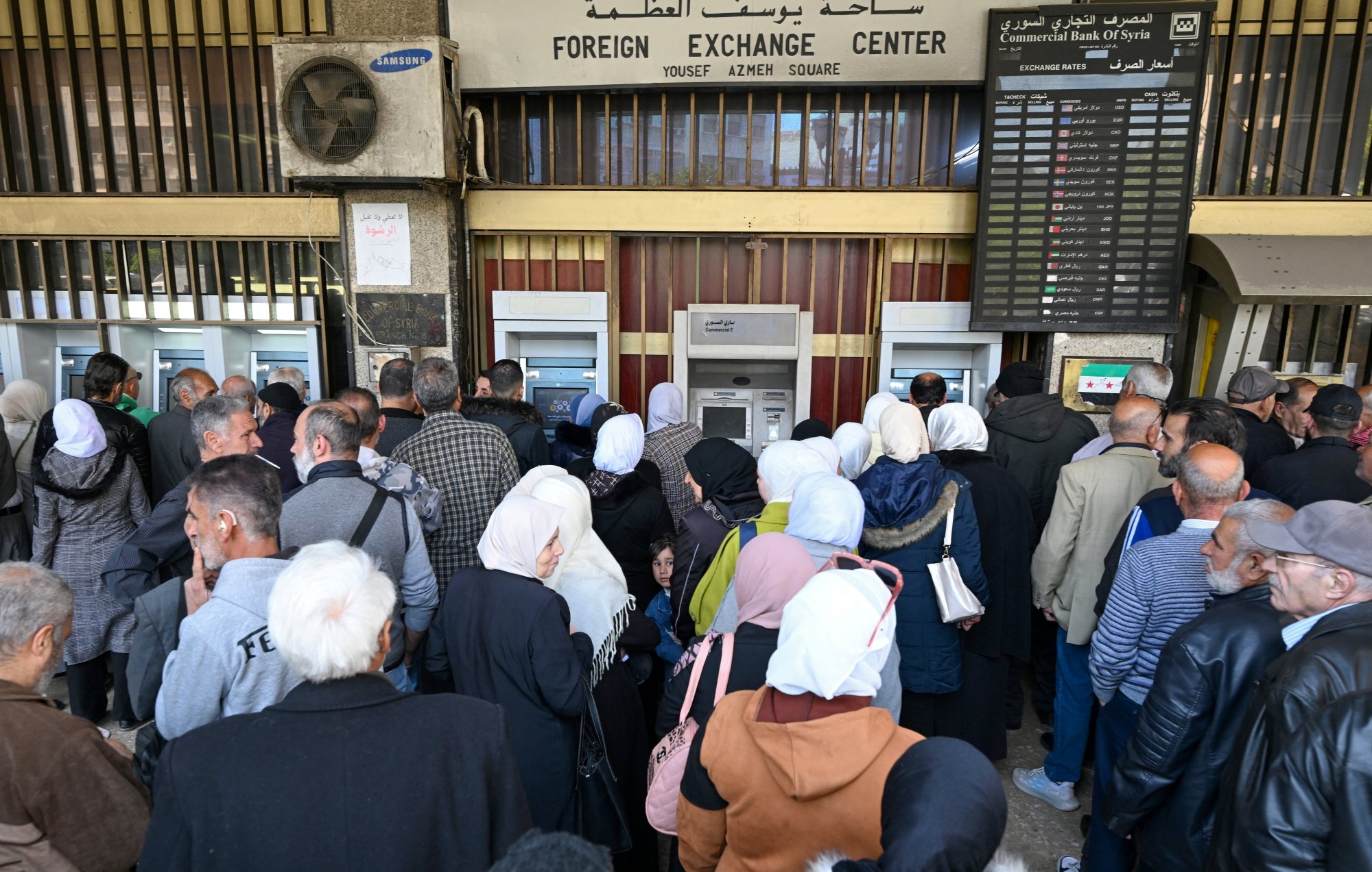 Une foule de personnes fait la queue devant un guichet bancaire.