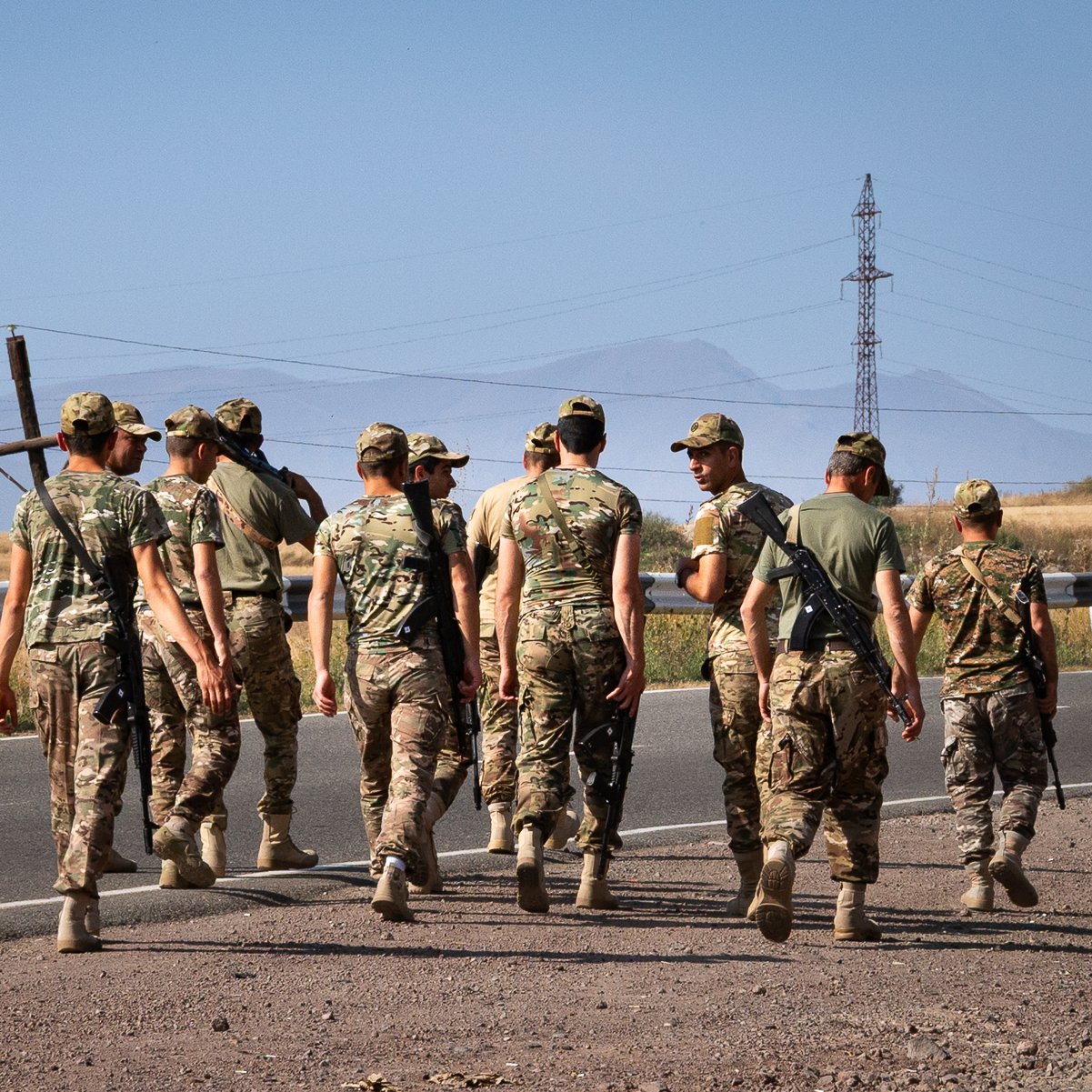 Des soldats marchent en groupe sur une route, avec des montagnes en arrière-plan.