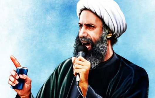 L'image représente un homme en train de parler avec passion. Il porte une tenue traditionnelle noire et un turban blanc. Dans sa main, il tient un petit objet, et il semble s'adresser à une foule ou à un public. Son expression faciale montre une intensité et une détermination. L'arrière-plan est d'un bleu léger, ce qui met en valeur sa silhouette.