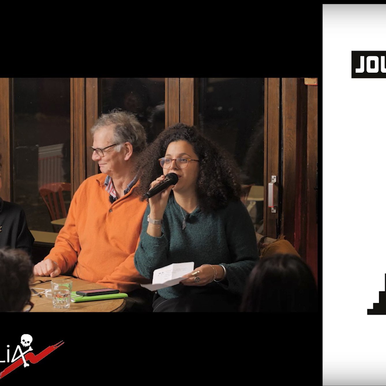 Nell'immagine si vede un gruppo di persone sedute a una tavola, probabilmente in un evento o una discussione. Una donna è in piedi con un microfono, mentre gli altri collaboratori ascoltano attentamente. Sul lato destro, c'è una copertina di un libro intitolato "Journal de Bord de Gaza", con un design stilizzato che rappresenta degli edifici e un elemento grafico che potrebbe simboleggiare la situazione nella regione. La scena trasmette un senso di impegno e dialogo.