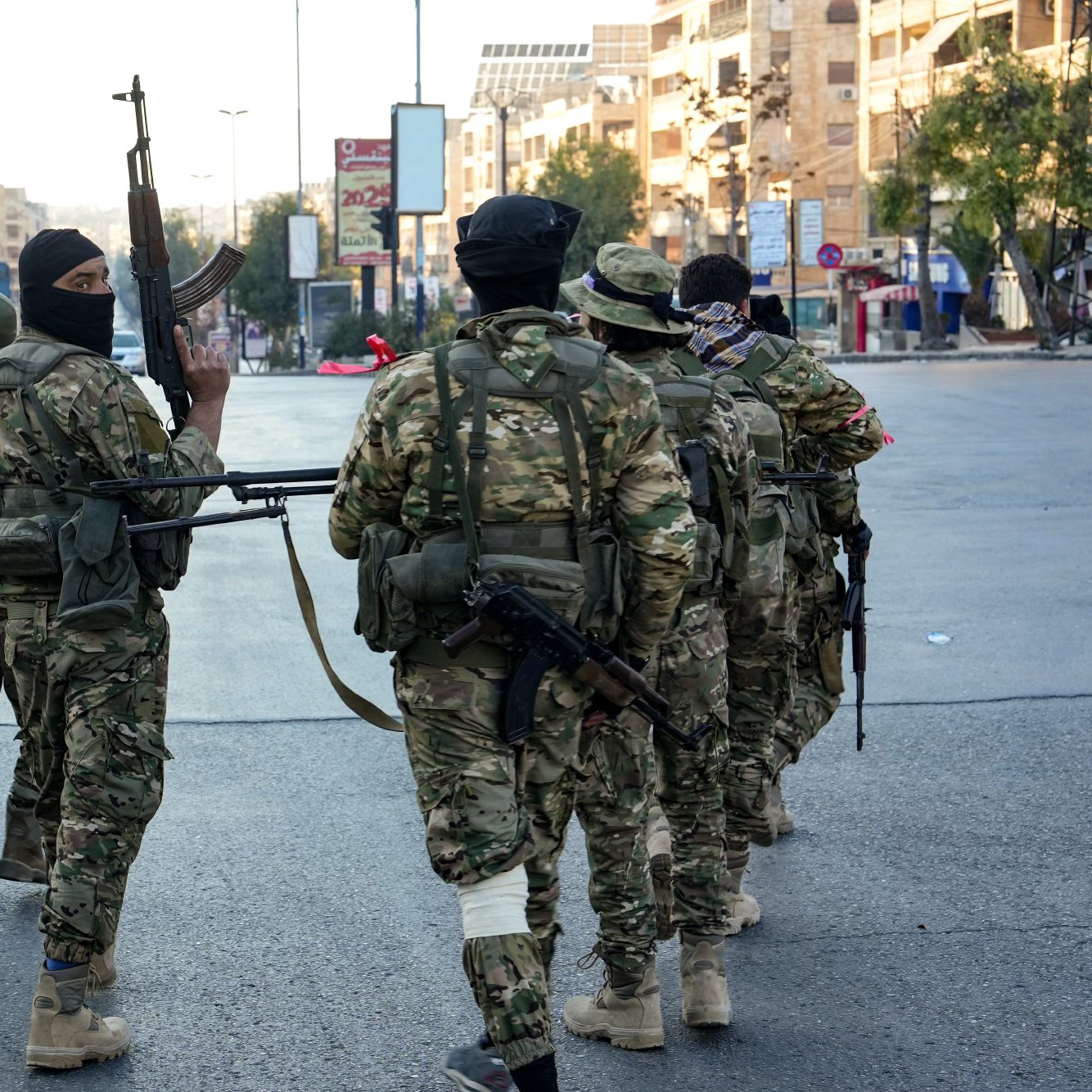 در این تصویر، تعدادی سرباز در یک خیابان urban دیده می‌شود. آن‌ها در حال راه رفتن به سمت دوربین هستند و برخی از آن‌ها سلاح‌های خود را در دست دارند. سربازان لباس‌های نظامی و کلاه‌خودهایی به سر دارند و برخی از آن‌ها صورت‌هایشان را با ماسک پوشانده‌اند. محیط اطراف آنها شامل ساختمان‌ها و خیابان‌های شلوغ است و به نظر می‌رسد در حال گشت‌زنی یا پاسداری از منطقه هستند.