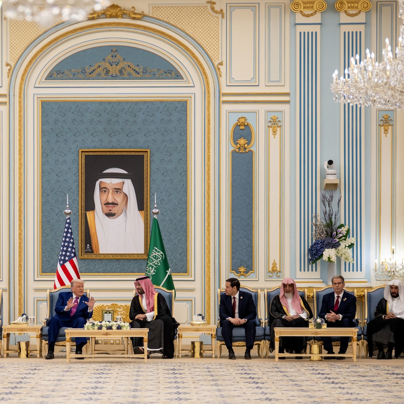A formal meeting with leaders seated in an ornate room, a large portrait on the wall.