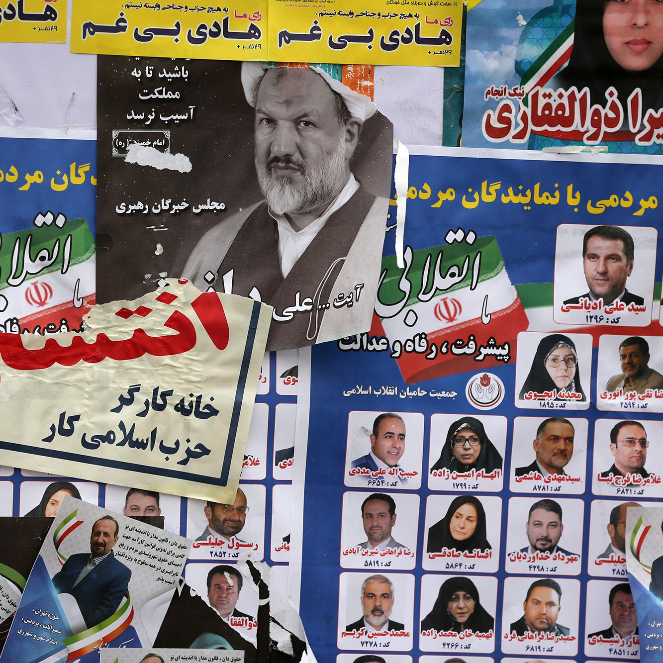 The image features a collage of colorful political posters and flyers. The posters display various candidates' photographs with names and party affiliations in both Persian and possibly Arabic. There's a prominent poster in the center that stands out, likely featuring a well-known figure, along with slogans related to an election, emphasizing themes of revolution and Islamic governance. The overall scene conveys a significant political campaign atmosphere, possibly in an Iranian context, with a mix of promotional materials for different candidates.