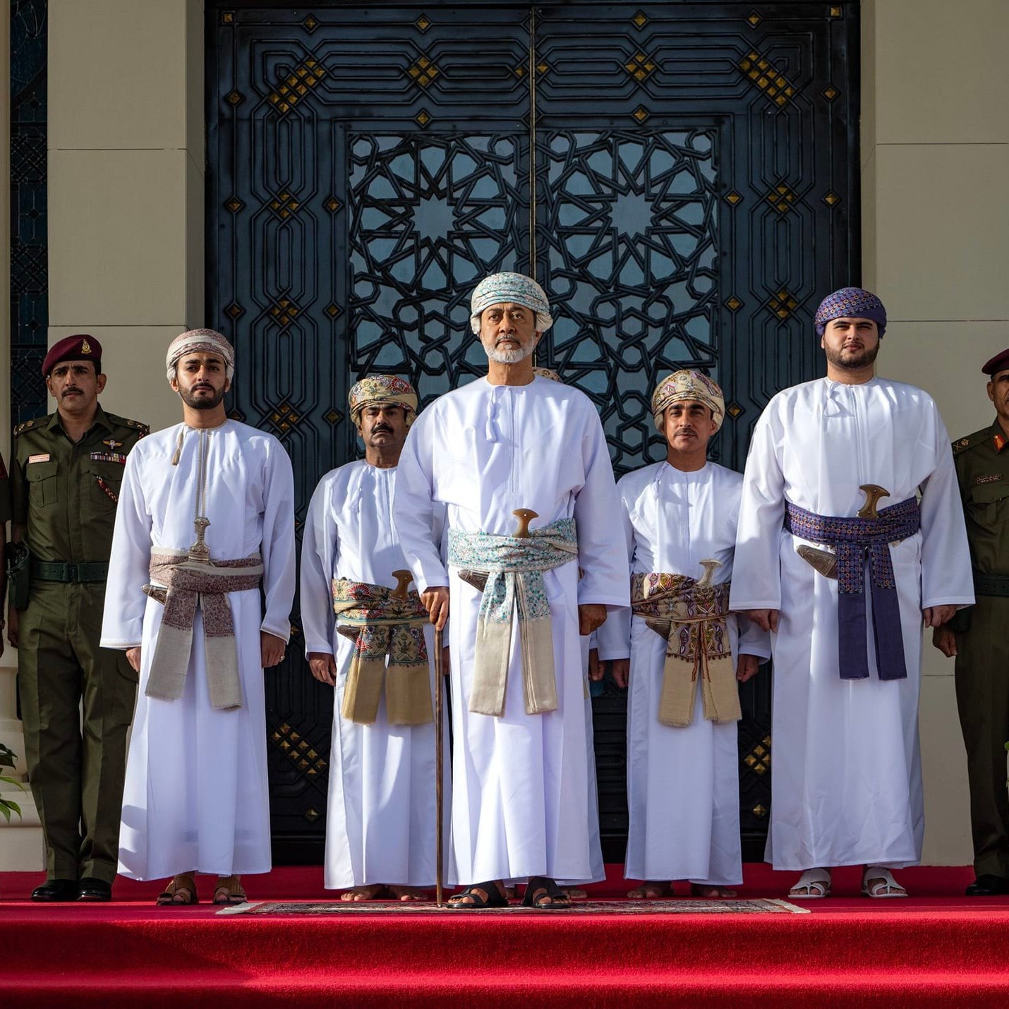 Groupe en tenues traditionnelles, debout devant un bâtiment orné, entouré de gardes.