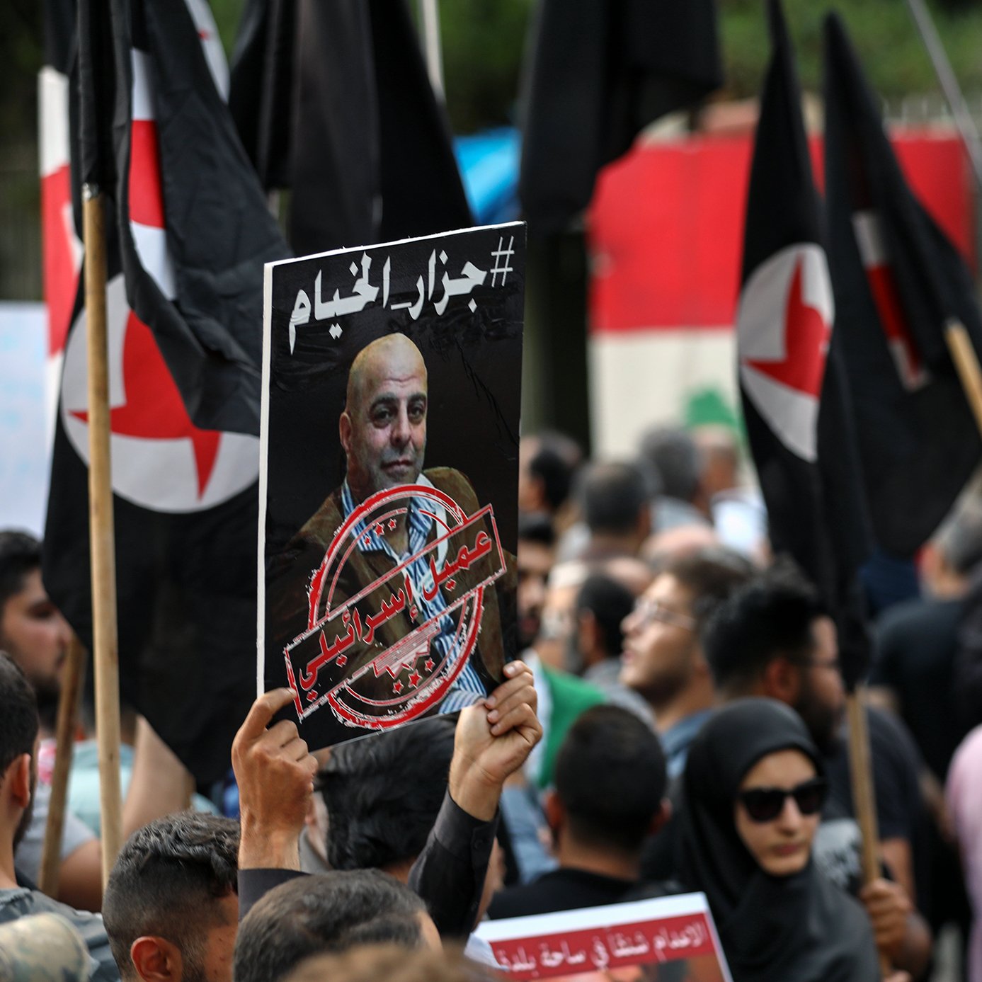 الصورة توضح تجمعًا حاشدًا حيث يحمل المتظاهرون لافتات تحمل عبارات وشعارات مختلفة. من بين اللافتات، توجد صور لشخص يبدو أنه شخصية بارزة، مع وجود علامة تشير إلى معارضة أو احتجاج يتعلق بموضوع الإعدام. المتظاهرون يرتدون ملابس متنوعة، وبعضهم يحمل أعلامًا. الأجواء تعكس شعوراً بالاحتجاج والرفض.