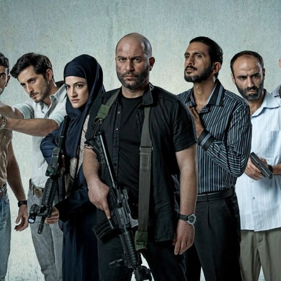 L'image montre un groupe de sept personnes armées, se tenant debout sur un fond gris. Ils ont des expressions déterminées et semblent en position de confrontation. Certains d'entre eux tiennent des armes à feu, tandis qu'une femme porte un hijab et se tient au milieu du groupe. Les hommes sont vêtus de vêtements variés, allant de casual à militaire. L'atmosphère est intense et pourrait suggérer un contexte d'action ou de tension.