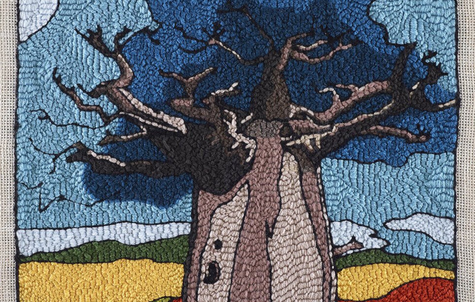 Un grand baobab aux branches nues, sous un ciel bleu, entouré de champs colorés.