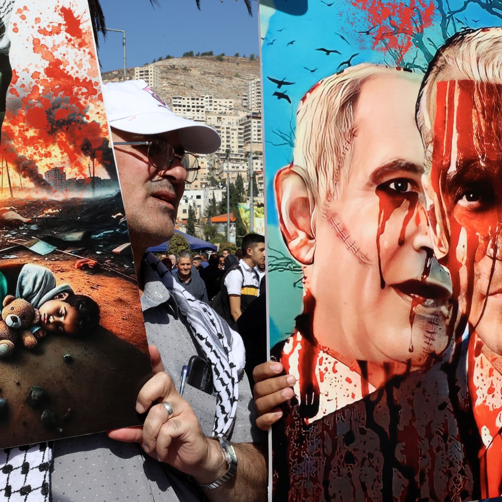 L'image montre des manifestants tenant des pancartes lors d'une démonstration. À gauche, une affiche illustre une scène tragique avec un enfant couché sur le sol, entouré de débris et d'une atmosphère de destruction. À droite, une illustration satirique ou critique représente deux figures, avec des visages peints évoquant des thèmes de violence, symbolisés par des éclaboussures de sang. L'ensemble évoque des questions politiques et humanitaires, avec un fort impact visuel.