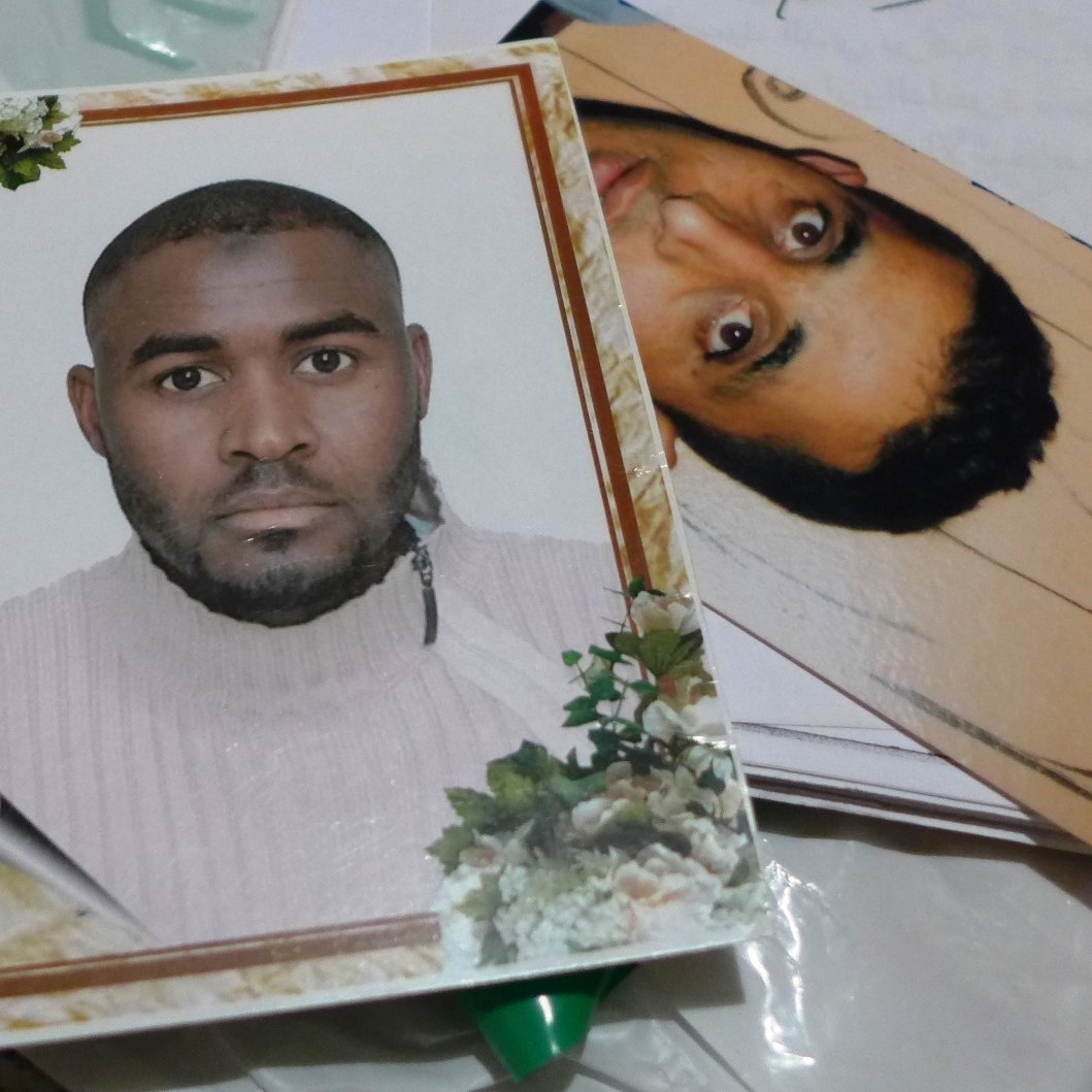 L'image montre des cartes ou des photos disposées sur une surface. À gauche, une photo d'un homme avec un pull léger et un fond décoré de fleurs. À droite, une autre photo d'un homme, son expression et son style étant différents. Les deux images semblent appartenir à des documents personnels ou des souvenirs.