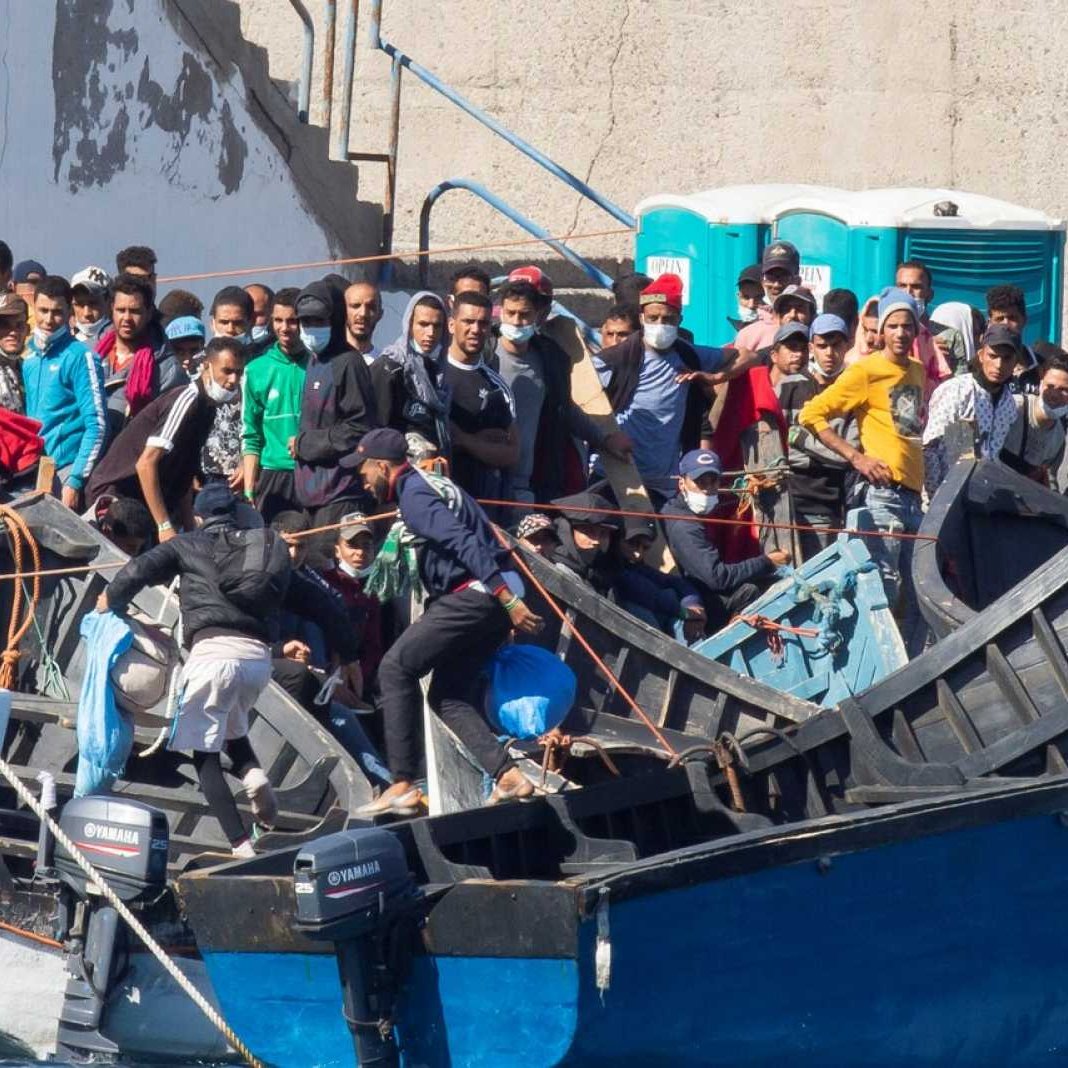 L'image montre un groupe de personnes sur des embarcations, probablement dans un port ou une zone côtière. Les individus semblent rassemblés autour de plusieurs bateaux, avec une diversité de vêtements, certains portant des masques. L'environnement est urbain, et il y a des structures en béton visibles en arrière-plan. On peut noter une atmosphère de mouvement et d'activité parmi les personnes présentes sur les bateaux.