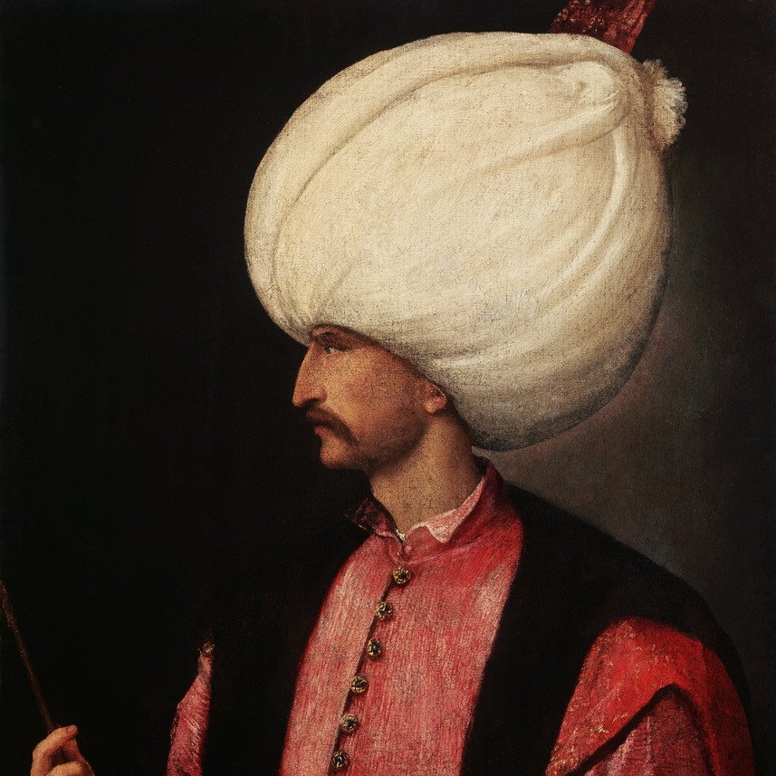 L'image représente un homme en profil, portant un turban blanc imposant. Il est habillé d'une tunique rose ornée de boutons et d'un veston noir, ce qui lui donne un aspect richement décoré. Son visage est finement dessiné, mettant en valeur sa moustache. Il tient un bâton dans une main, ce qui suggère une position de pouvoir ou d'autorité. L'arrière-plan est sombre, ce qui fait ressortir les détails de sa tenue et de son expression.