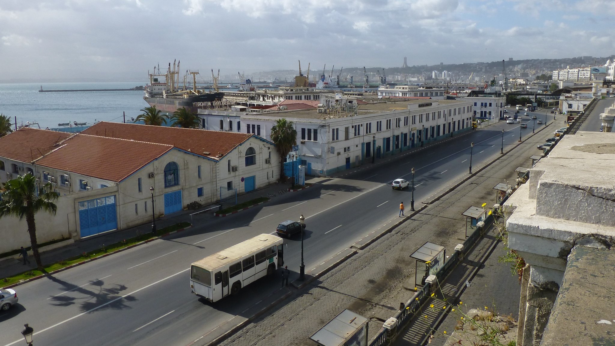 Vue d'une ville côtière avec des bâtiments, port et nuages. Ambiance calme et urbaine.