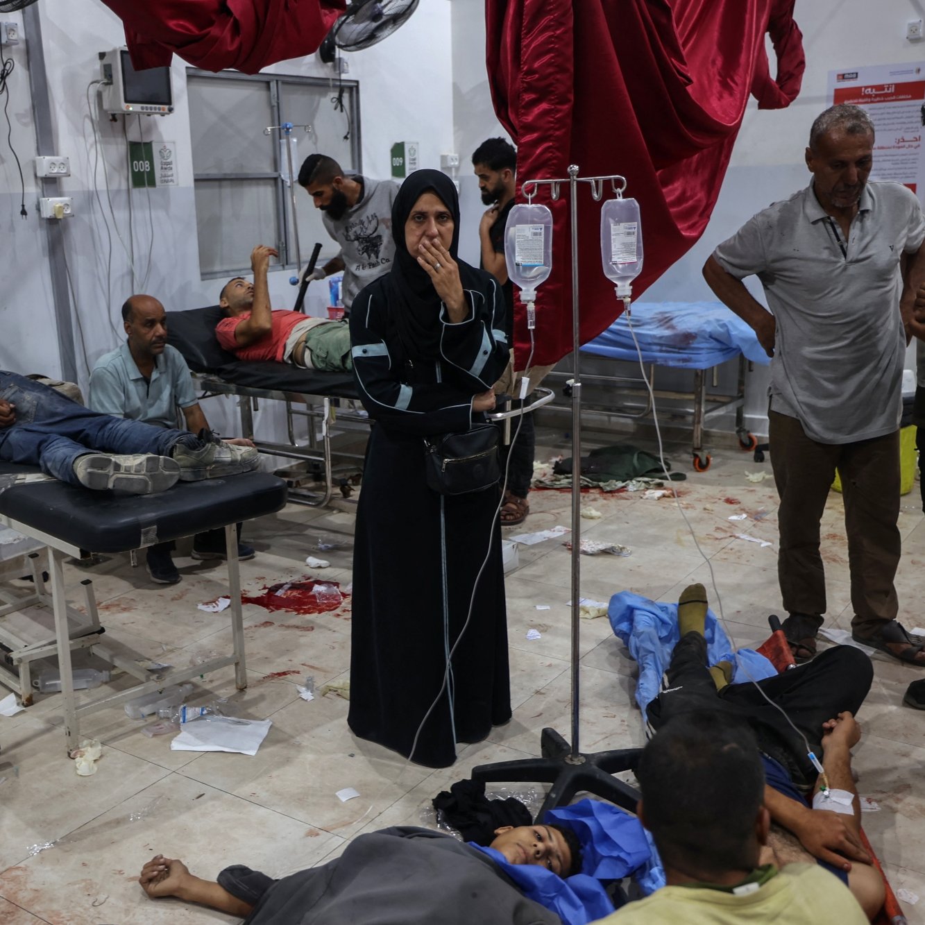 یک بیمارستان شلوغ با بیماران مصدوم درازکشیده و کادر پزشکی مشغول کمک‌رسانی. حالتی اضطراری و نگران‌کننده.