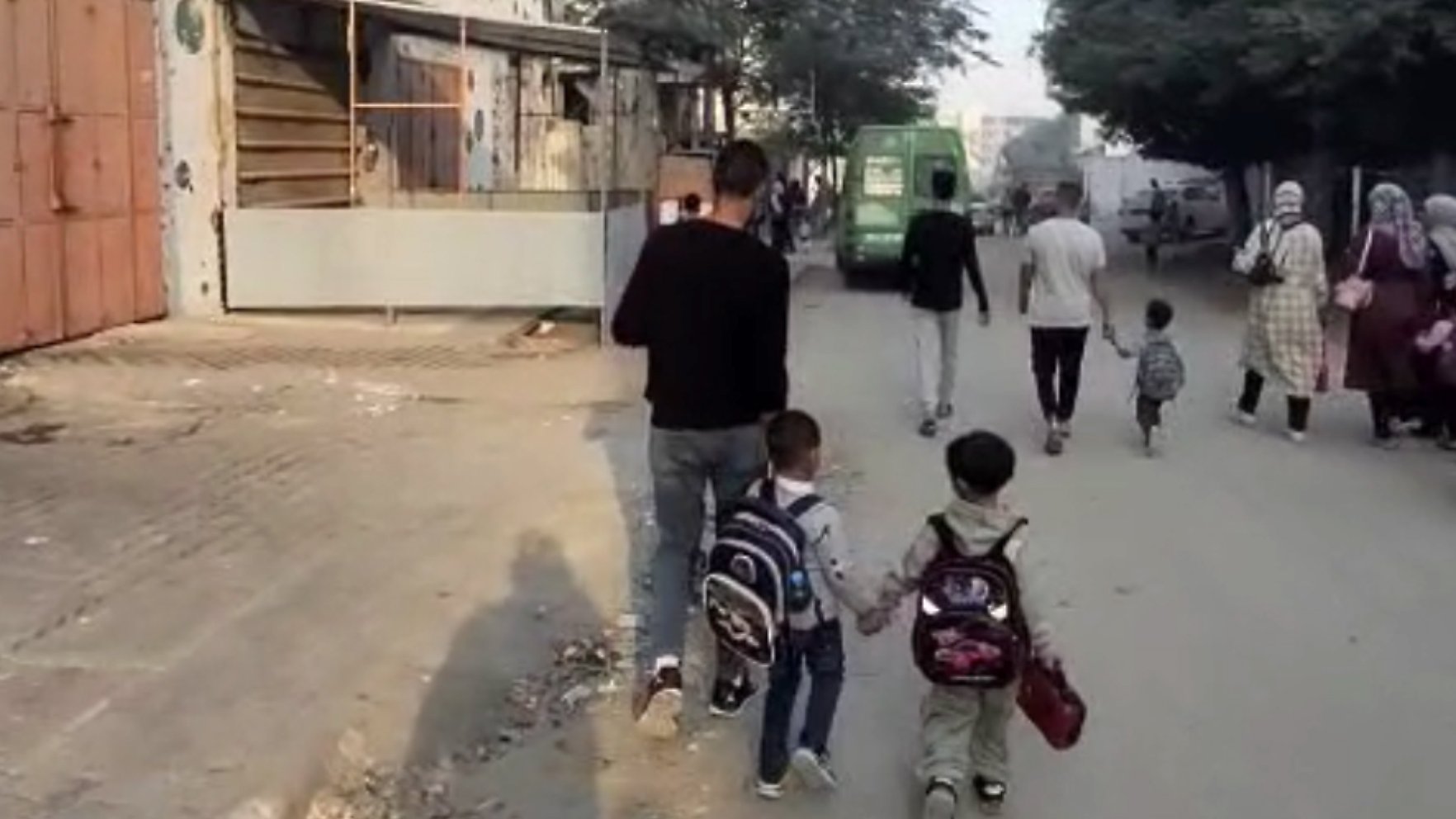 Des enfants marchent main dans la main avec un adulte sur une rue animée.