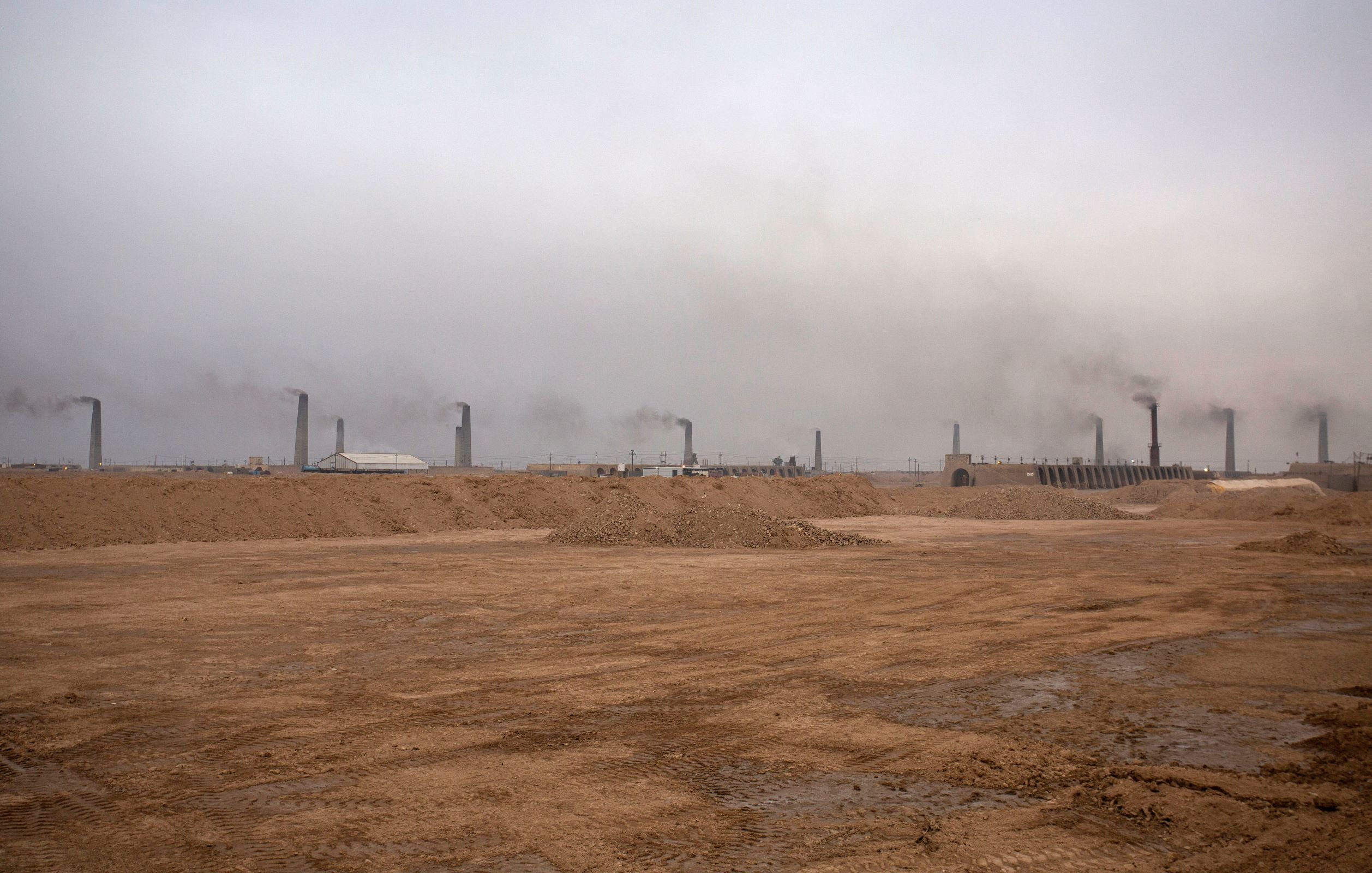 این تصویر یک محیط صنعتی را نشان می‌دهد که در آن دود از دودکش‌های بلند بیرون می‌آید. آسمان به طور کلی ابری و خاکستری به نظر می‌رسد و هوای منطقه آلوده است. زمین خاکی و خشک به نظر می‌رسد و هیچ گونه پوشش گیاهی قابل مشاهده نیست. این صحنه می‌تواند نشان‌گر فعالیت‌های صنعتی و مشکلات زیست‌محیطی باشد.