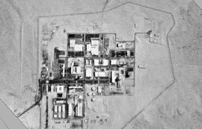 L'image montre une vue aérienne en noir et blanc d'une installation industrielle ou militaire située dans une zone désertique. On peut y voir plusieurs bâtiments et structures disposés de manière ordonnée, entourés d'une clôture ou d'une barrière. Le paysage environnant semble aride, avec peu de végétation visible. Cette configuration suggère un site ayant des activités techniques ou de recherche avancées.