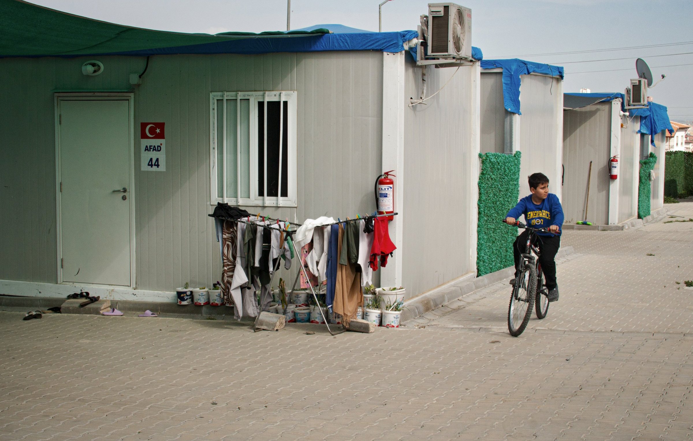 Un enfant à vélo passe près de cabines modulaires et de vêtements accrochés.