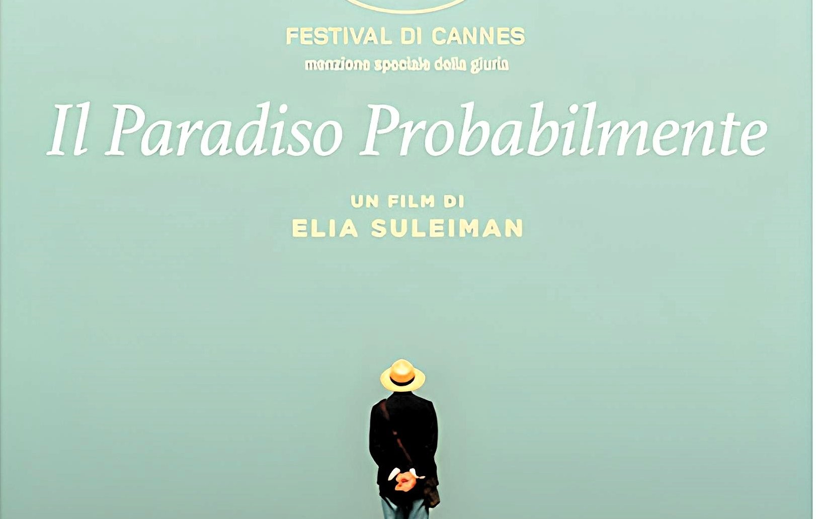 L'immagine sembra rappresentare un poster di un film intitolato "It Must Be Heaven", diretto da Elia Suleiman. In primo piano, c'è una figura umana di spalle, vestita con abiti leggeri e un cappello, che si trova su una scogliera e osserva l'orizzonte. Sullo sfondo, si vede un cielo sereno e un mare blu, creando un'atmosfera di tranquillità e contemplazione. Il titolo del film e il nome del regista sono scritti in caratteri chiari, dando risalto alla scena.