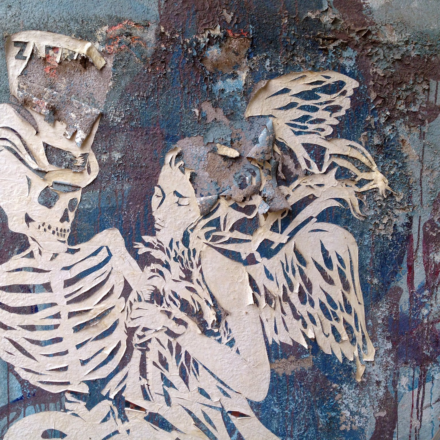 این تصویر نشان‌دهنده یک اثر هنری خیابانی است که شامل دو شخصیت است. در سمت چپ، یک اسکلت دیده می‌شود که به نظر می‌رسد در حال برقراری ارتباط با شخص دیگری است. این شخصیت دیگر یک زن بال‌دار است که به آرامی در کنار اسکلت قرار گرفته است. هر دو شخصیت به صورت کُنده و با جزئیات محدود و رنگ‌های ملایم نمایش داده شده‌اند. پس‌زمینه تصویر نیز با رنگ‌های فرسوده و طرح‌های انتزاعی پوشانده شده که حس قدیمی و هنری خاصی دارد.