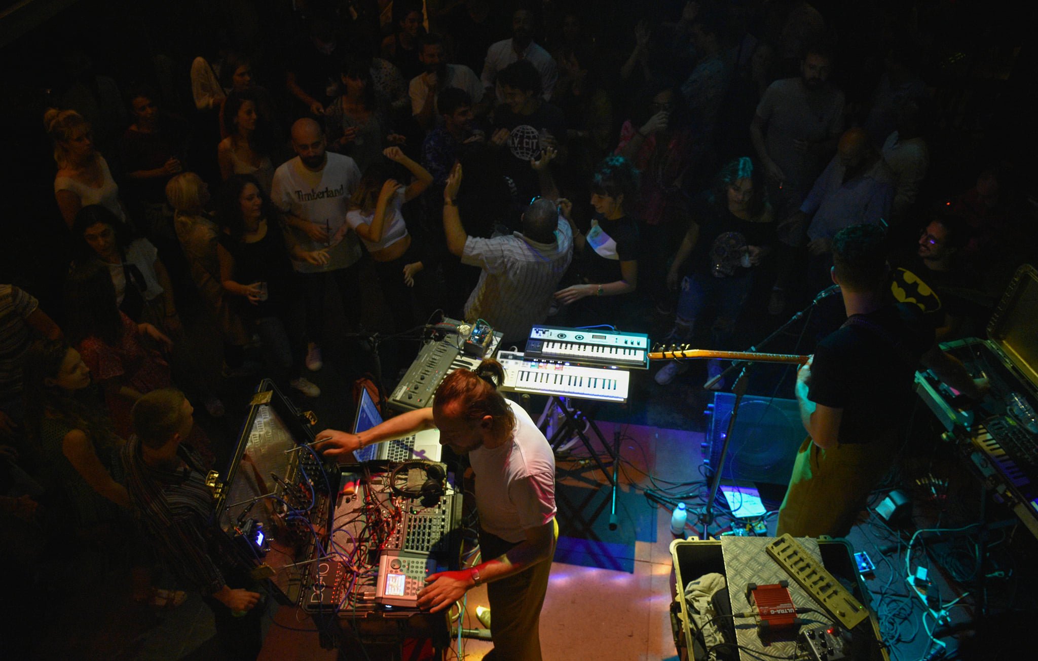 A lively crowd enjoys live music from performers with electronic instruments on stage.