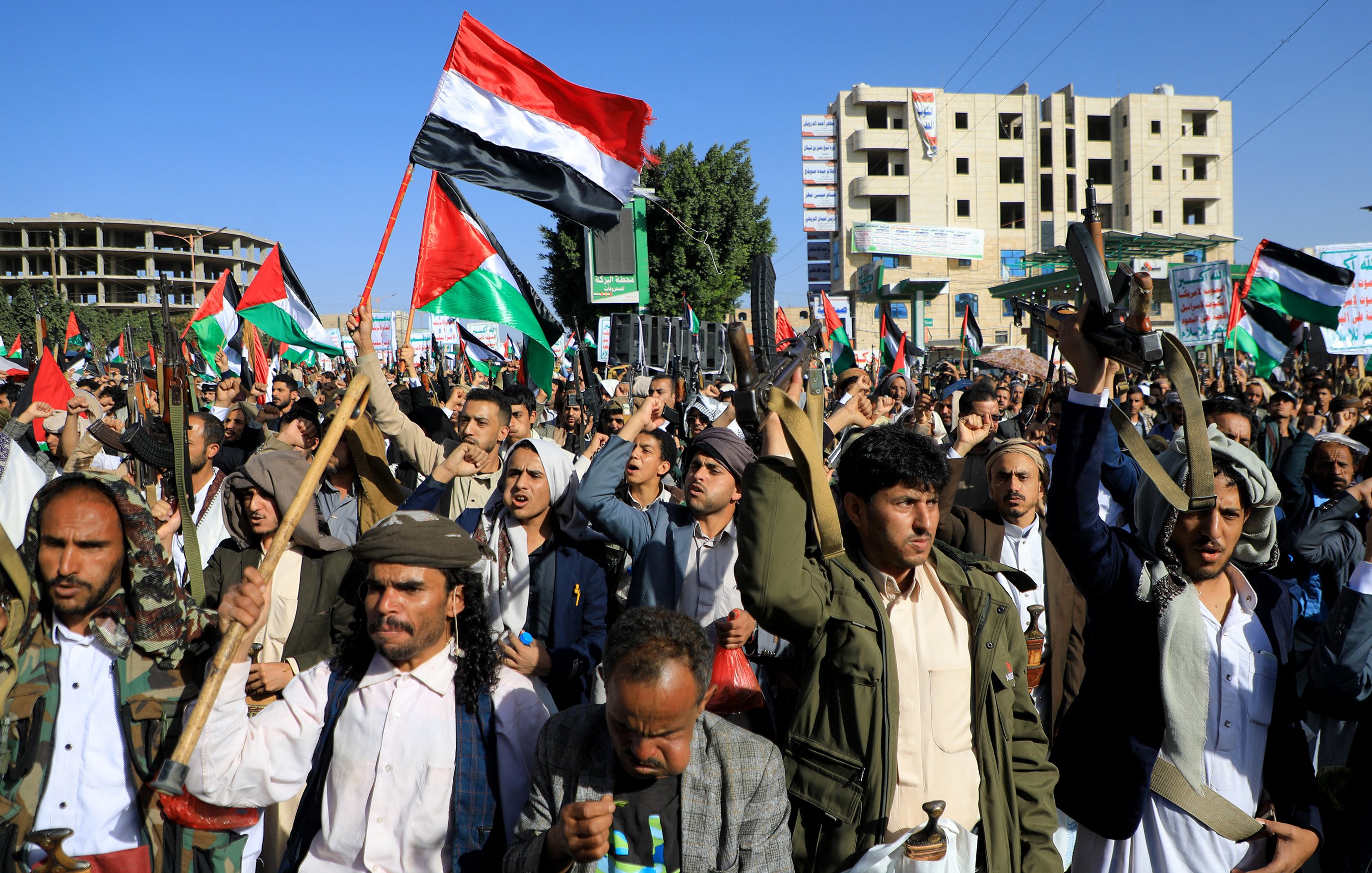 تظهر الصورة مجموعة من الأشخاص في تظاهرة حاشدة، يحملون الأعلام ويرتدون زيًّا تقليديًا. تعبر الوجوه عن الحماس وتظهر الأعلام التي تحمل ألوان الوطن. تتواجد خلفهم بنايات وبعض العلامات التجارية، مما يوحي بأن المكان هو منطقة حضرية. يبدو أن المتظاهرين يمارسون حقهم في التعبير عن آرائهم والمشاركة في حدث سياسي أو اجتماعي.