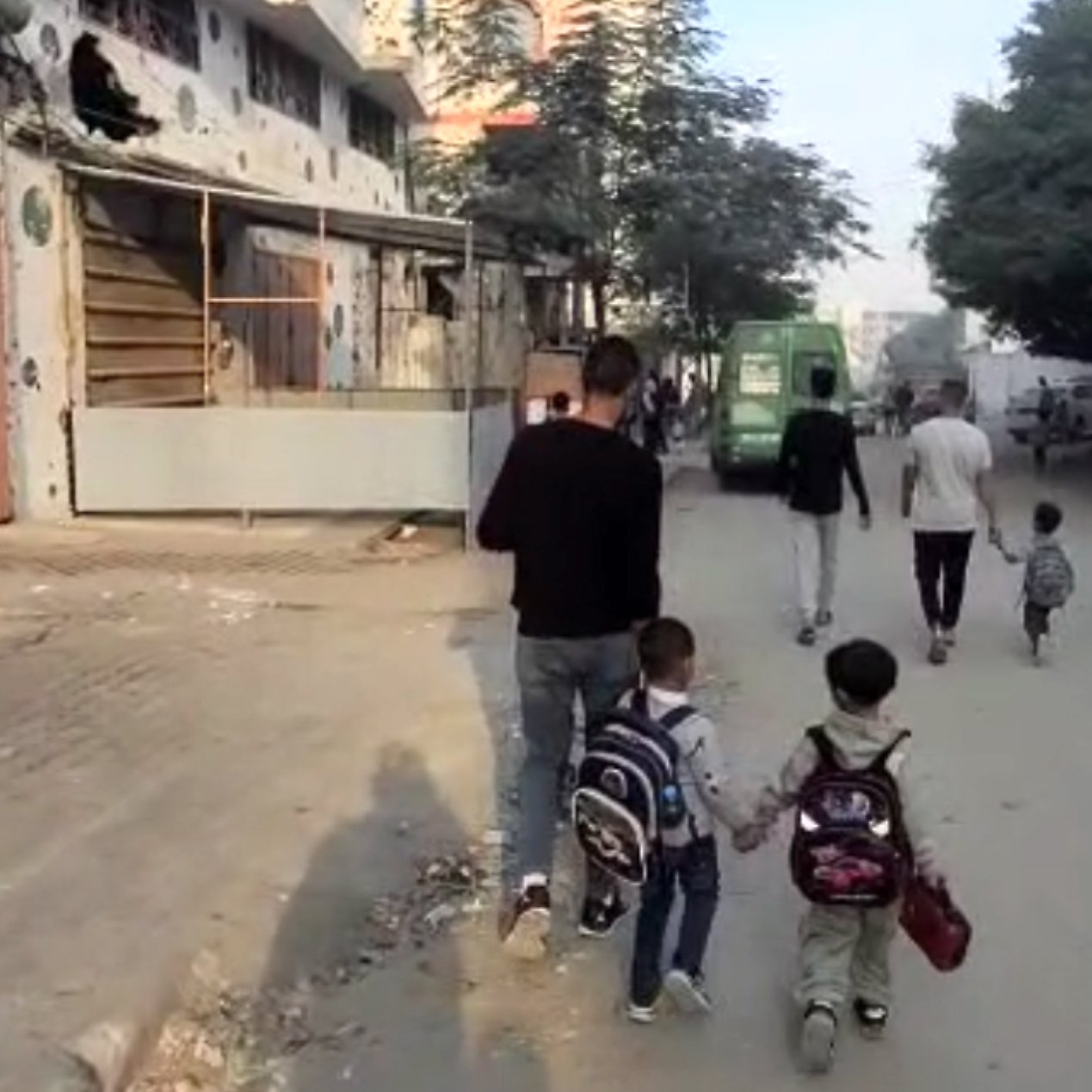Des enfants marchent main dans la main avec un adulte sur une rue animée.