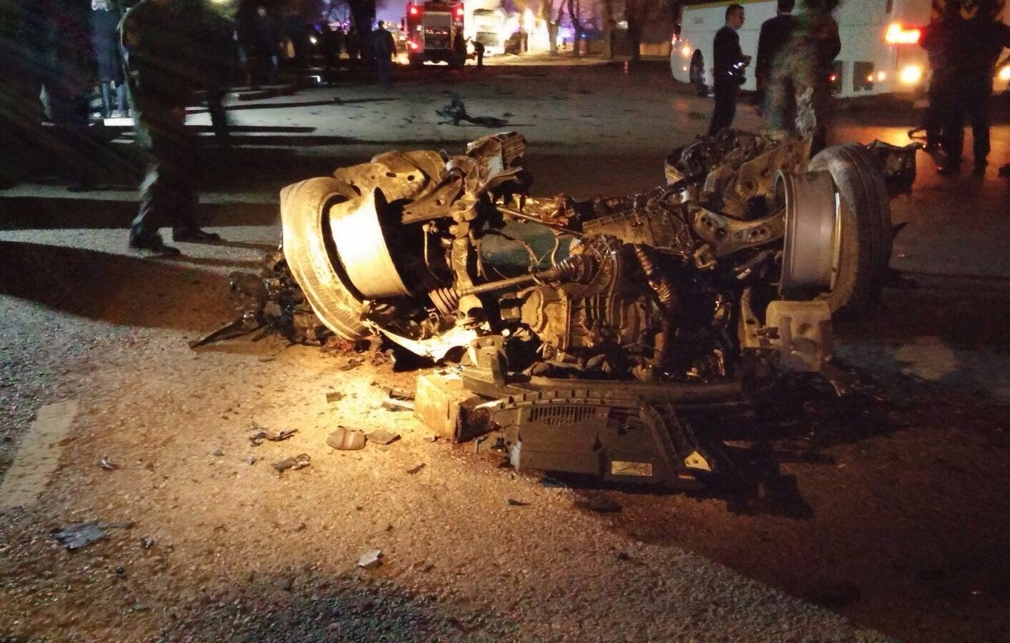 تصویر نشان‌دهنده یک تصادف خودرو است که در آن یک خودرو به طور کامل واژگون شده و روی سقف خود قرار دارد. قطعات خودرو به اطراف پخش شده و آسیب‌های قابل توجهی به آن وارد شده است. صحنه روشنایی کمی دارد و ممکن است در یک شب یا در شرایط کم نور باشد. همچنین، افرادی در پس‌زمینه دیده می‌شوند که احتمالاً در حال رسیدگی به وضعیت هستند.