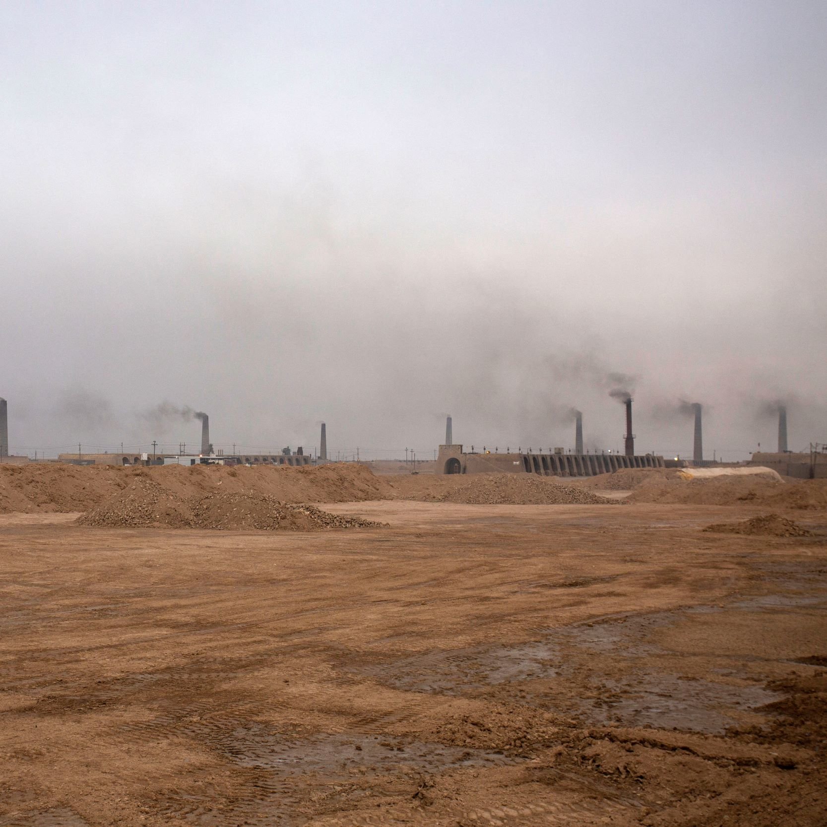 این تصویر یک محیط صنعتی را نشان می‌دهد که در آن دود از دودکش‌های بلند بیرون می‌آید. آسمان به طور کلی ابری و خاکستری به نظر می‌رسد و هوای منطقه آلوده است. زمین خاکی و خشک به نظر می‌رسد و هیچ گونه پوشش گیاهی قابل مشاهده نیست. این صحنه می‌تواند نشان‌گر فعالیت‌های صنعتی و مشکلات زیست‌محیطی باشد.