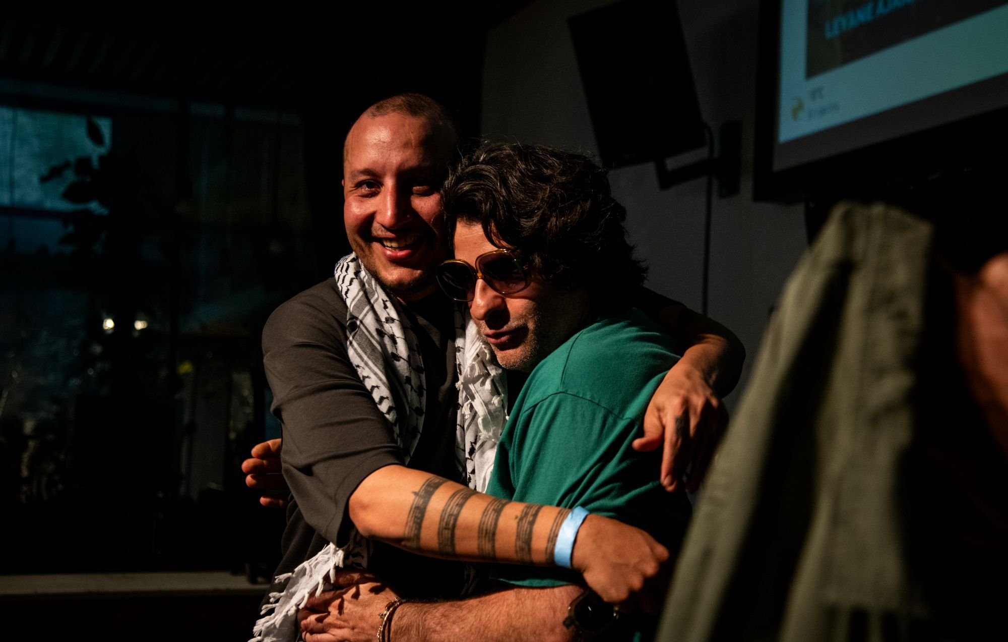 Deux hommes s'étreignent, souriants, avec des déguisements et un ambiance chaleureuse.