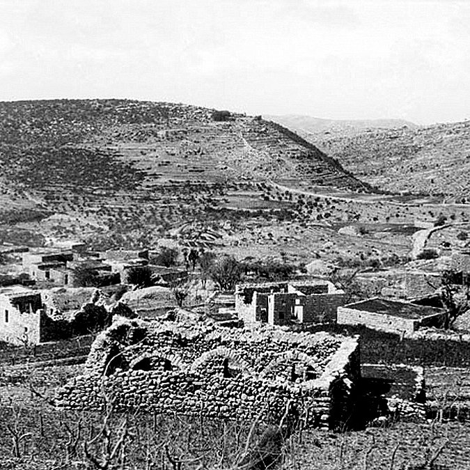 L'image montre un paysage rural en noir et blanc, où l'on peut apercevoir des ruines de structures en pierre, témoignant d'une ancienne habitation. Le terrain est vallonné, avec des collines en arrière-plan et une végétation clairsemée. Certaines zones semblent cultivées ou utilisées pour l'élevage, tandis que d'autres présentent des traces de dégradation ou d'abandon. L'atmosphère générale est paisible, mais elle évoque également une histoire de déclin ou de dévastation.