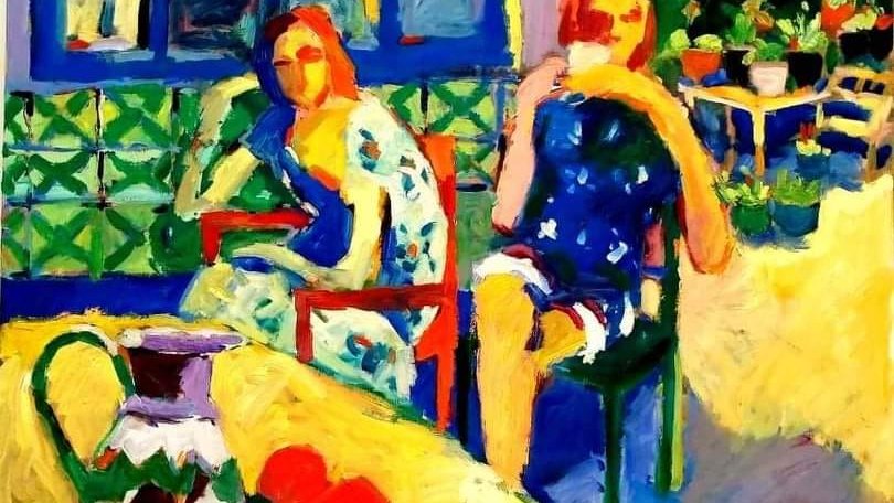 L'image présente une scène vibrante et colorée, avec deux femmes assises sur des chaises. L'une porte une robe bleu foncé, tandis que l'autre est vêtue d'une robe à motifs floraux. Le fond montre une fenêtre avec des carreaux colorés et un jardin verdoyant. Au premier plan, une table est dressée avec un pot et des fruits, ajoutant une touche vivante à la composition. Les couleurs sont éclatantes, donnant une impression de chaleur et de convivialité.